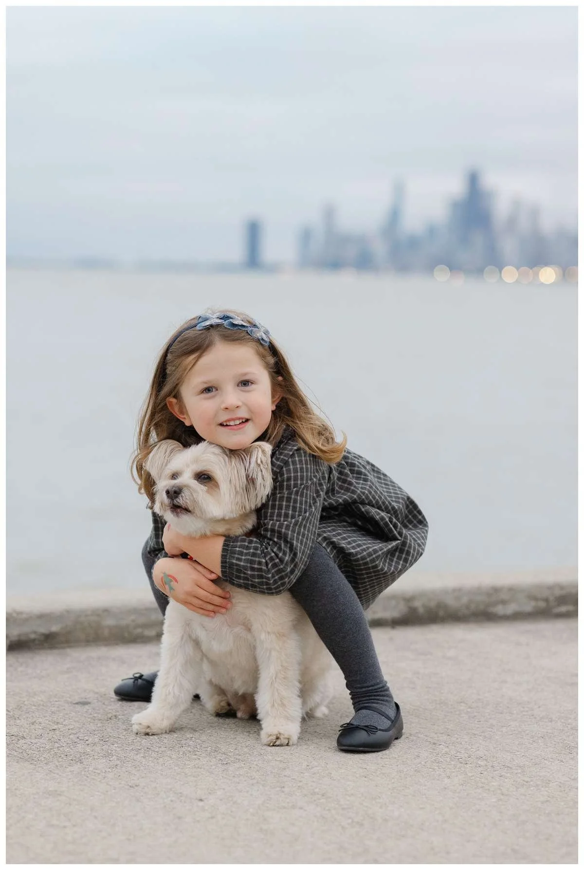 Girl hugging small white dog against the Chicago skyline by Chicago Photographer