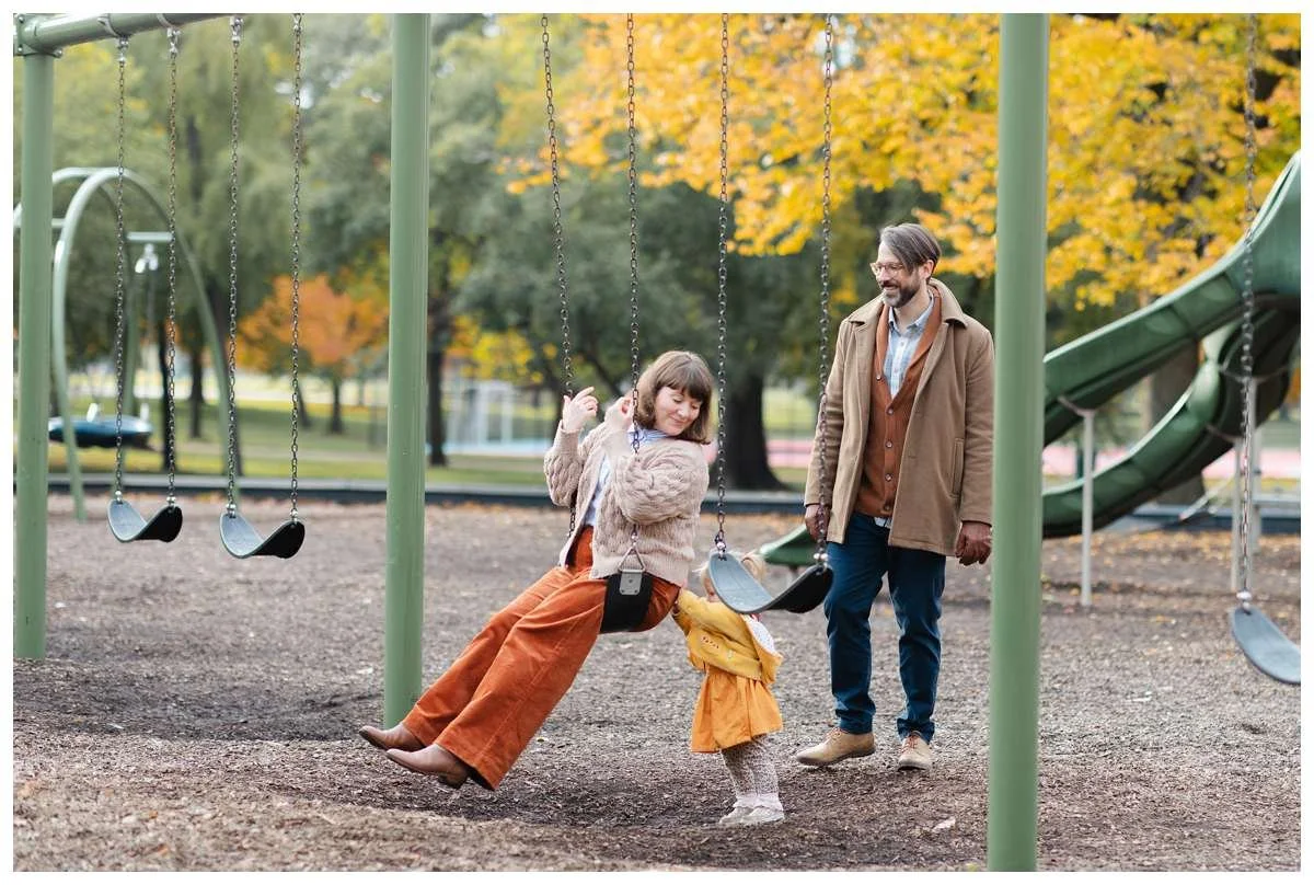 Little girl pushing a swing that her mom is sitting in