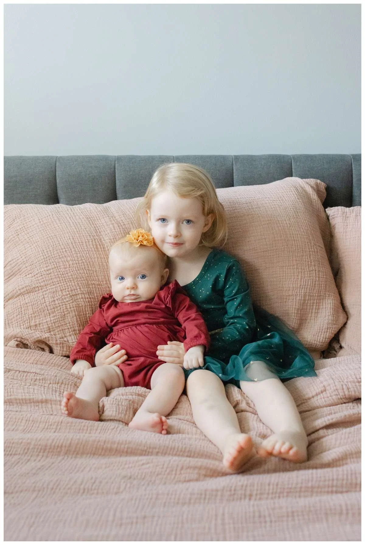 Two little sisters sitting on a bed and smiling