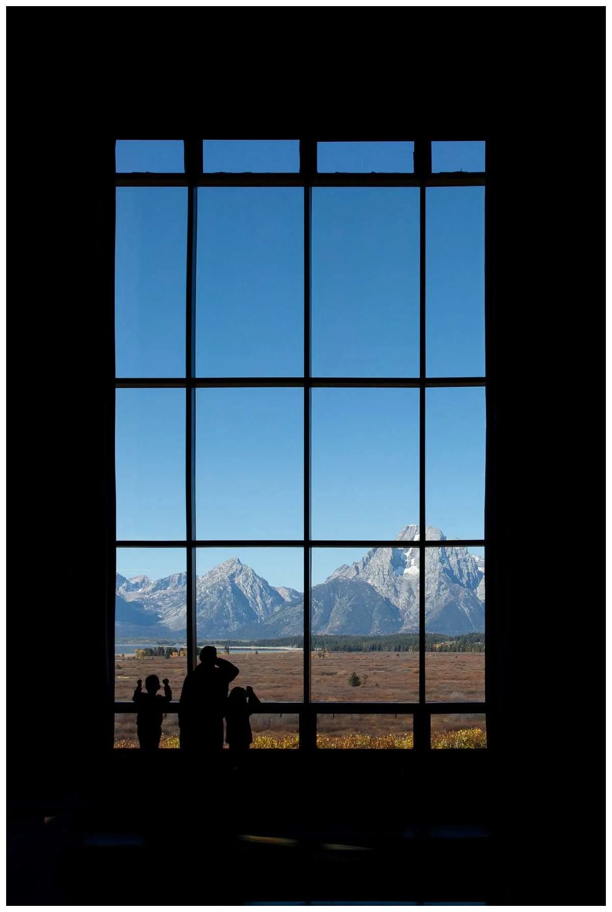 Family looking out window to mountains and blue skies at Jackson Lake Lodge, Grand Teton National Park