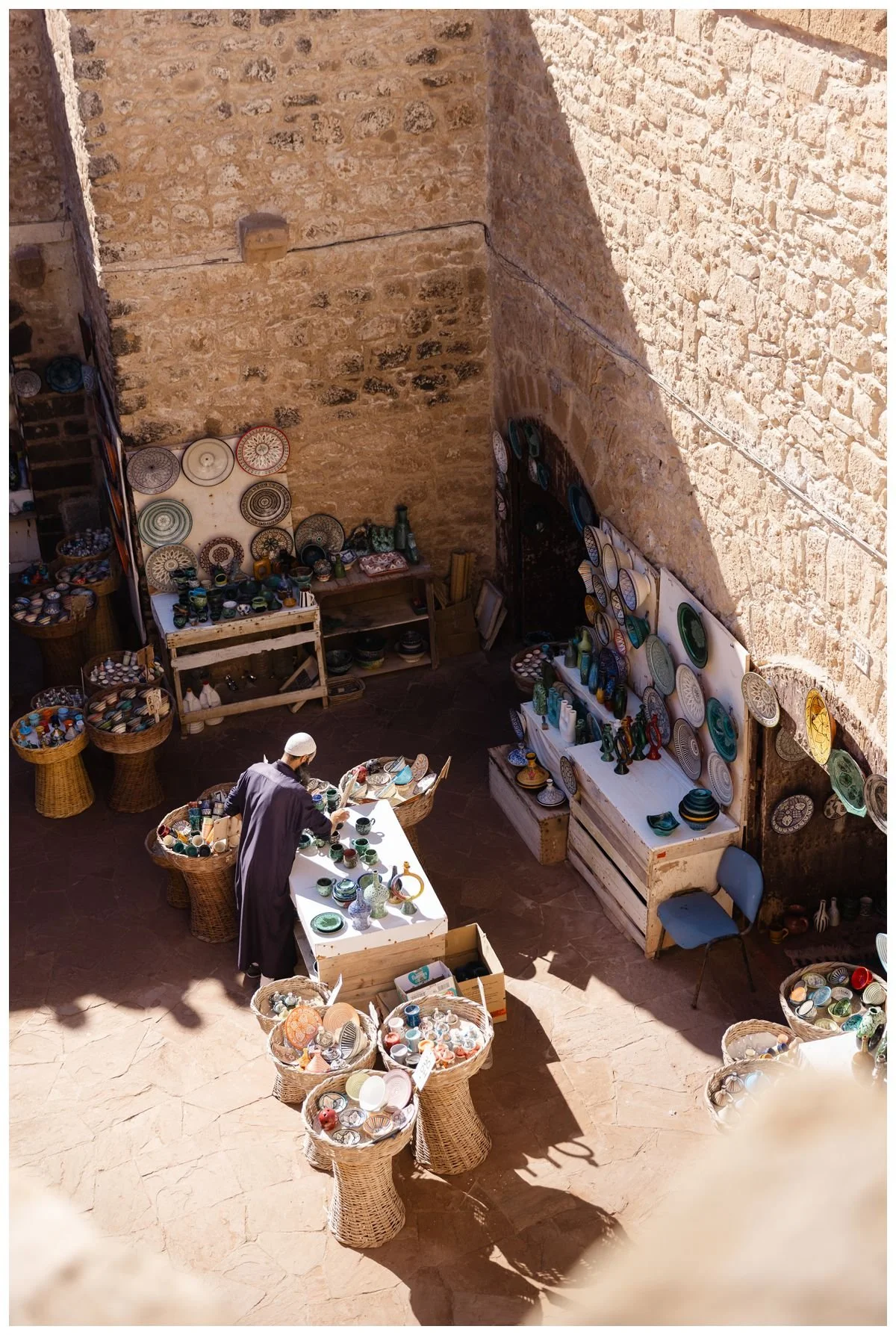 Man in traditional Moroccan garment arranging products for sale in Essaouri