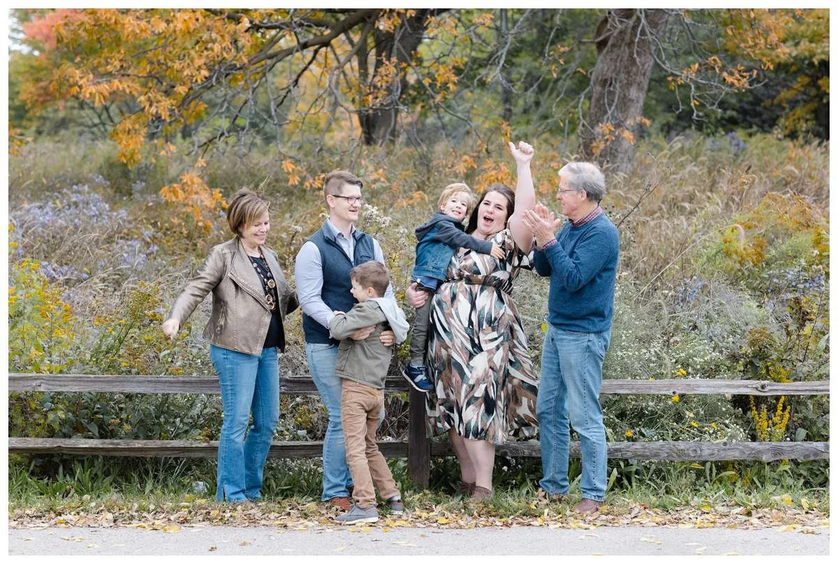 Extended family of parents, two children and grandparents cheering against colorful foliage in a Chicago Fall Family Session