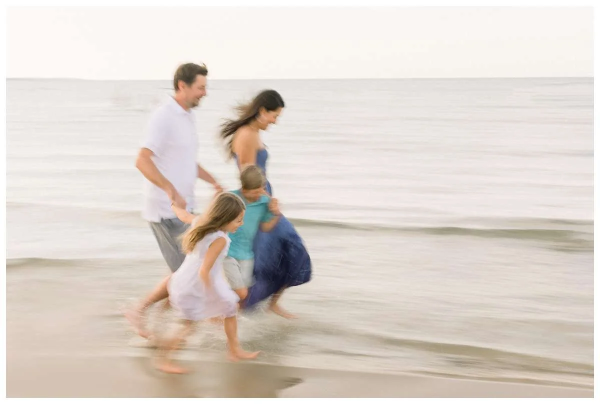 Blurry image of parents and kids running along a beach at sunset