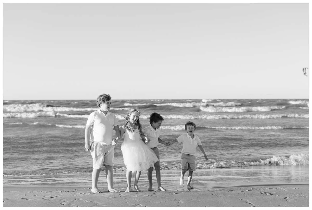 Four siblings holding hands and being playful on the shores of Lake Michigan for a beach photo session