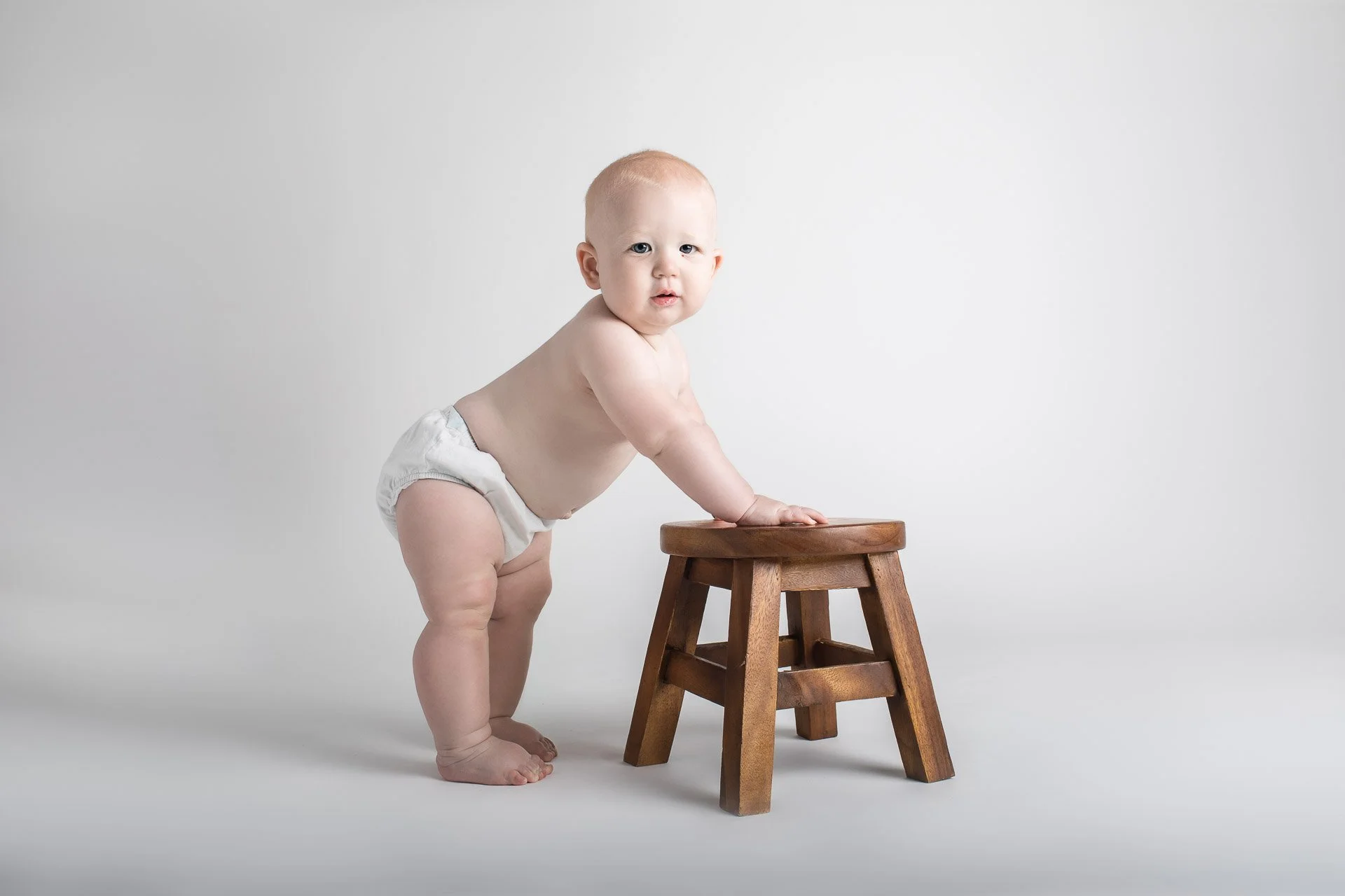 Studio milestone image of baby standing up aided by stool