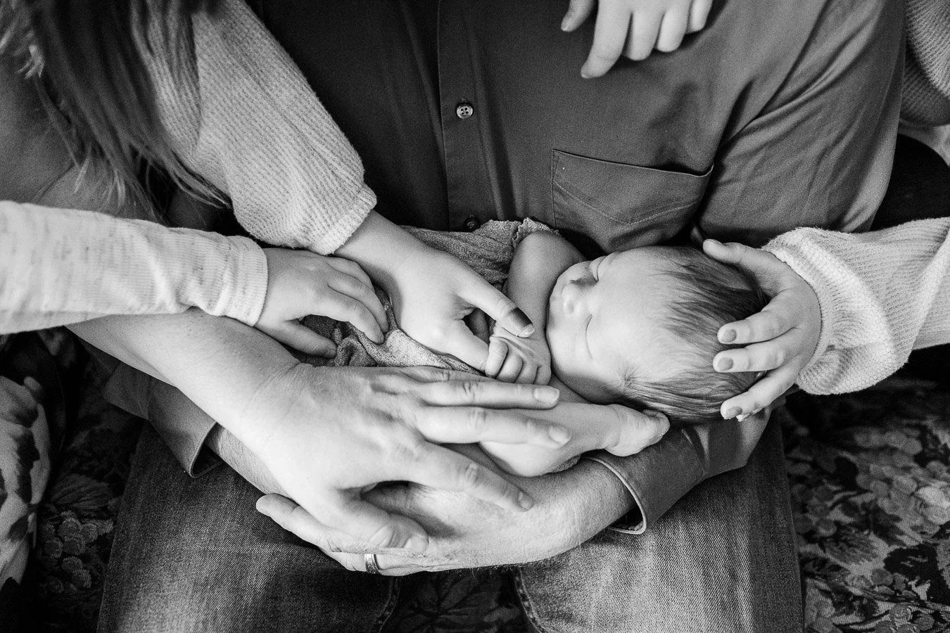 Father holding baby son while mom and three siblings touch its head, hands and feet