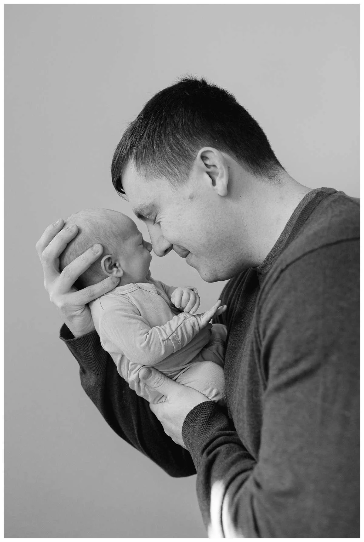 Profile image of father holding baby boy while they touch noses by Chicago Newborn Photographer