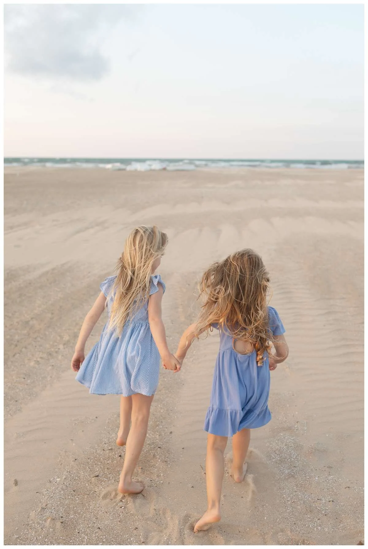 Girls running towards the beach while holding hands by Chicago Family Photographer