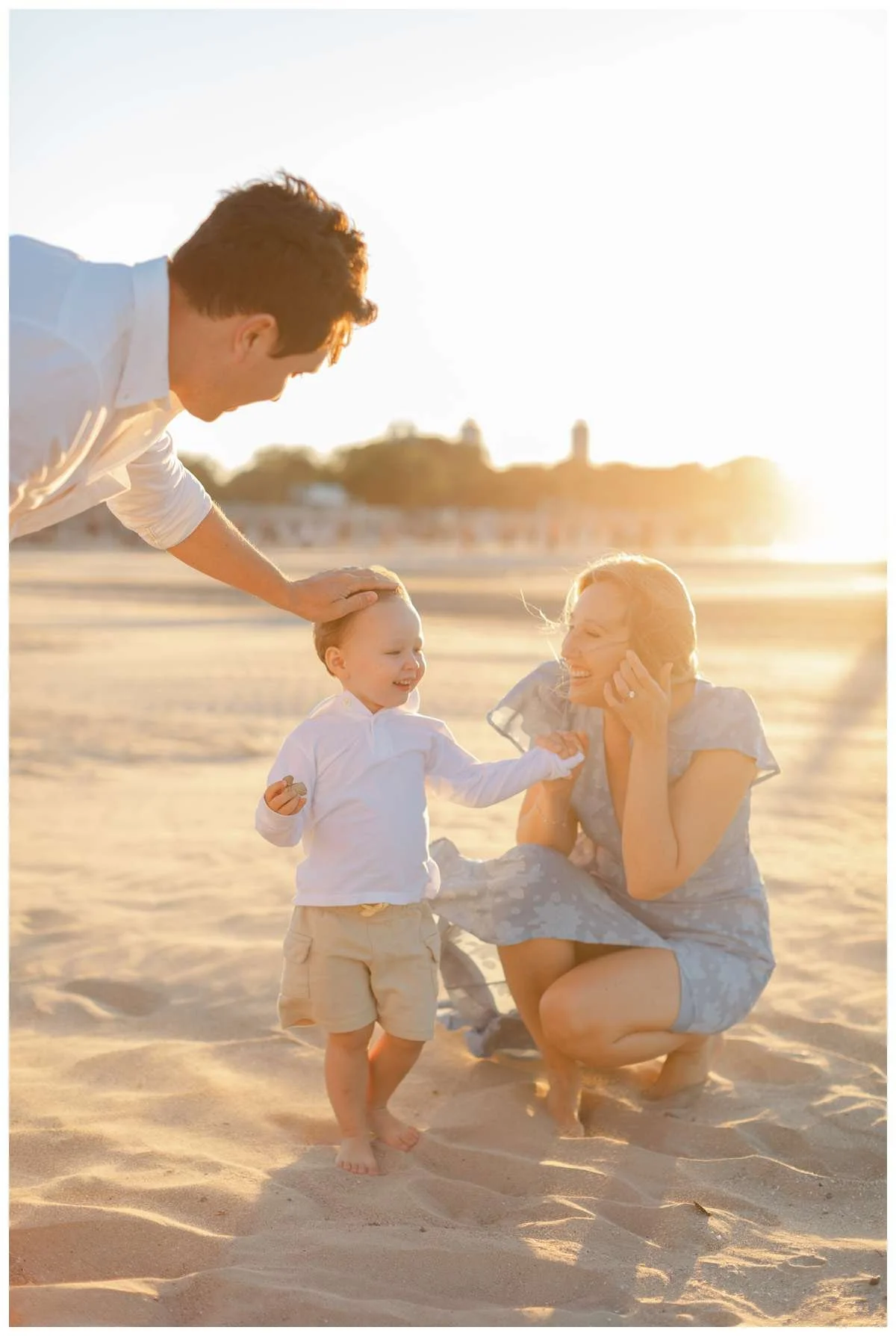Dad touching boys head while mom kneels next to him at Montrose Beach during golden hour