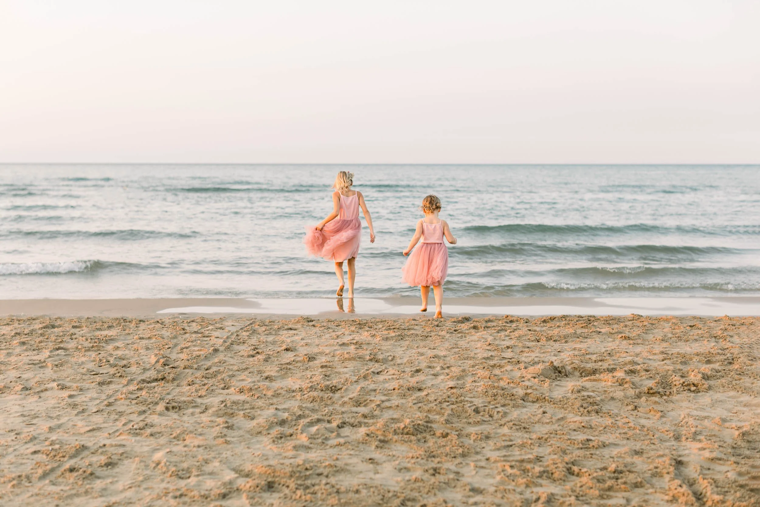 Sisters in pink tutus running towards Lake Michigan at golden hour by Chicago Family Photographer