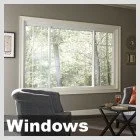 A window with a view of trees outside, with a black armchair and a wooden table nearby.
