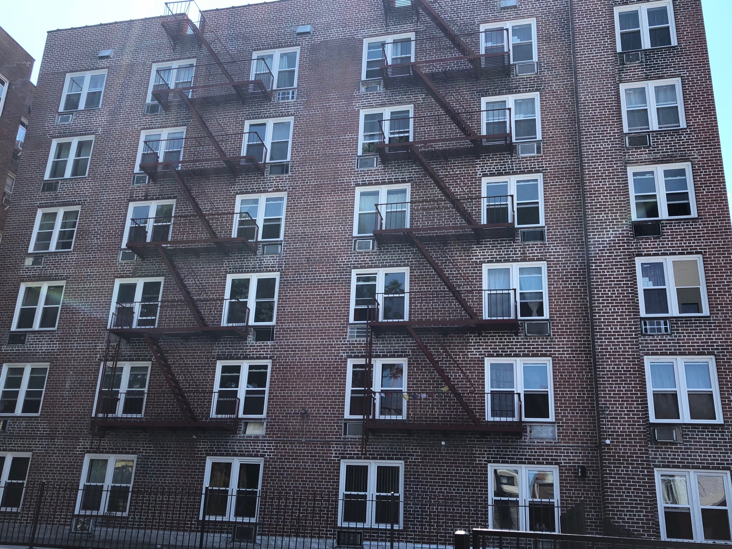 A multi-story brick apartment building with several windows and fire escape balconies.