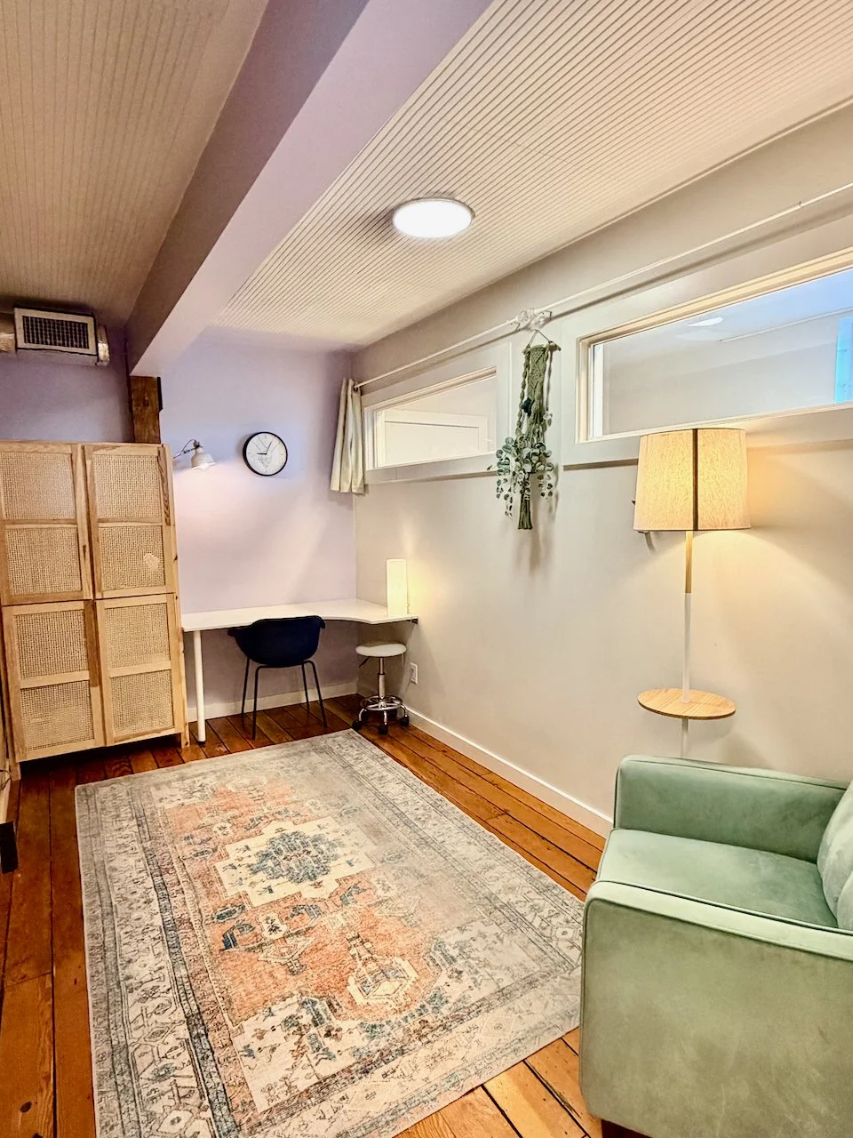  Bodywork bed for rent: There is a pillow at the head of the bed, a wooden cabinet with a plant on top, a standing cart with toiletries, a large mirror, and a window with light-colored curtains.