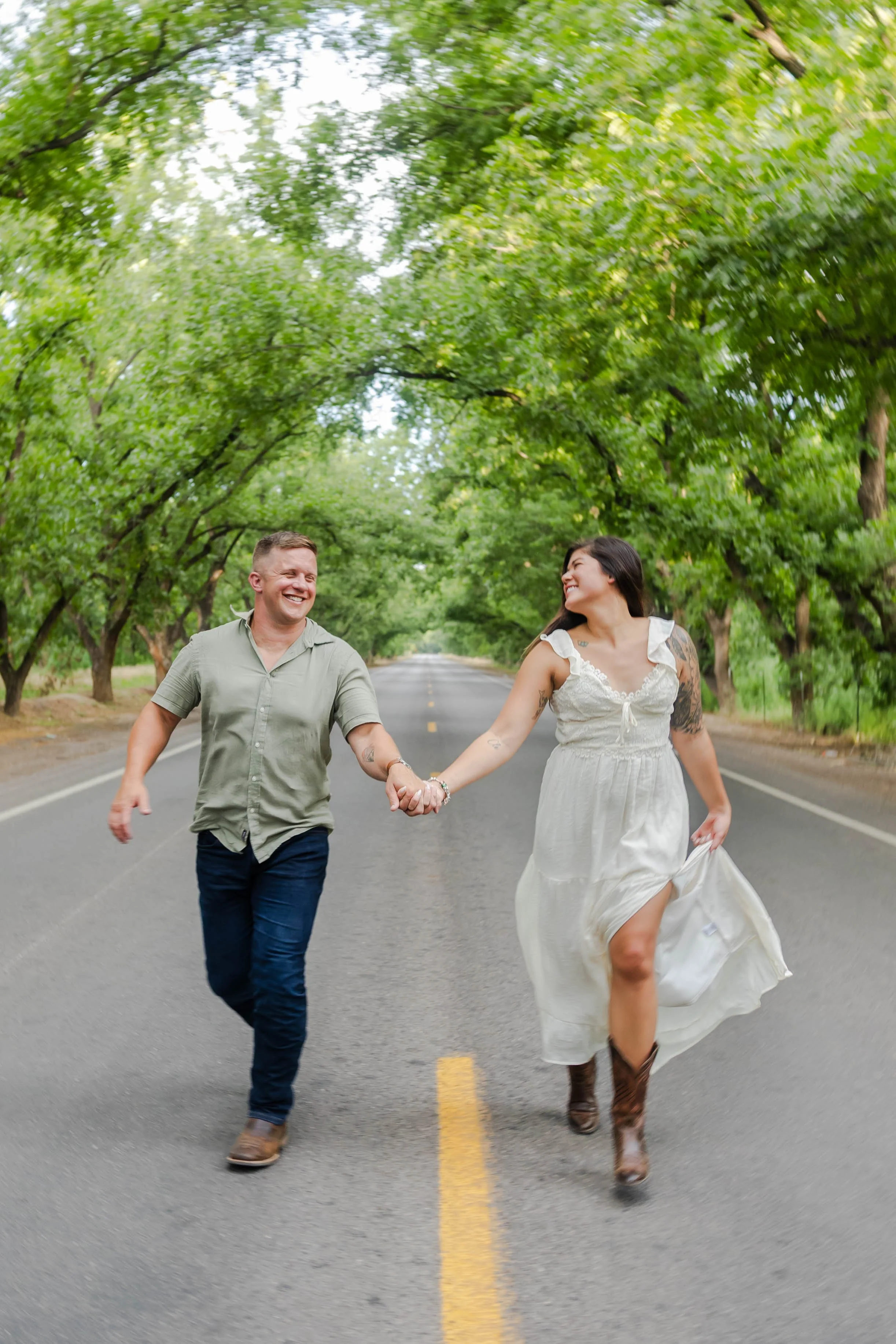 A man and woman holding hands and running on an empty rural road while walking across Southern New Mexico's Mesilla Valley Pecan Trees.
