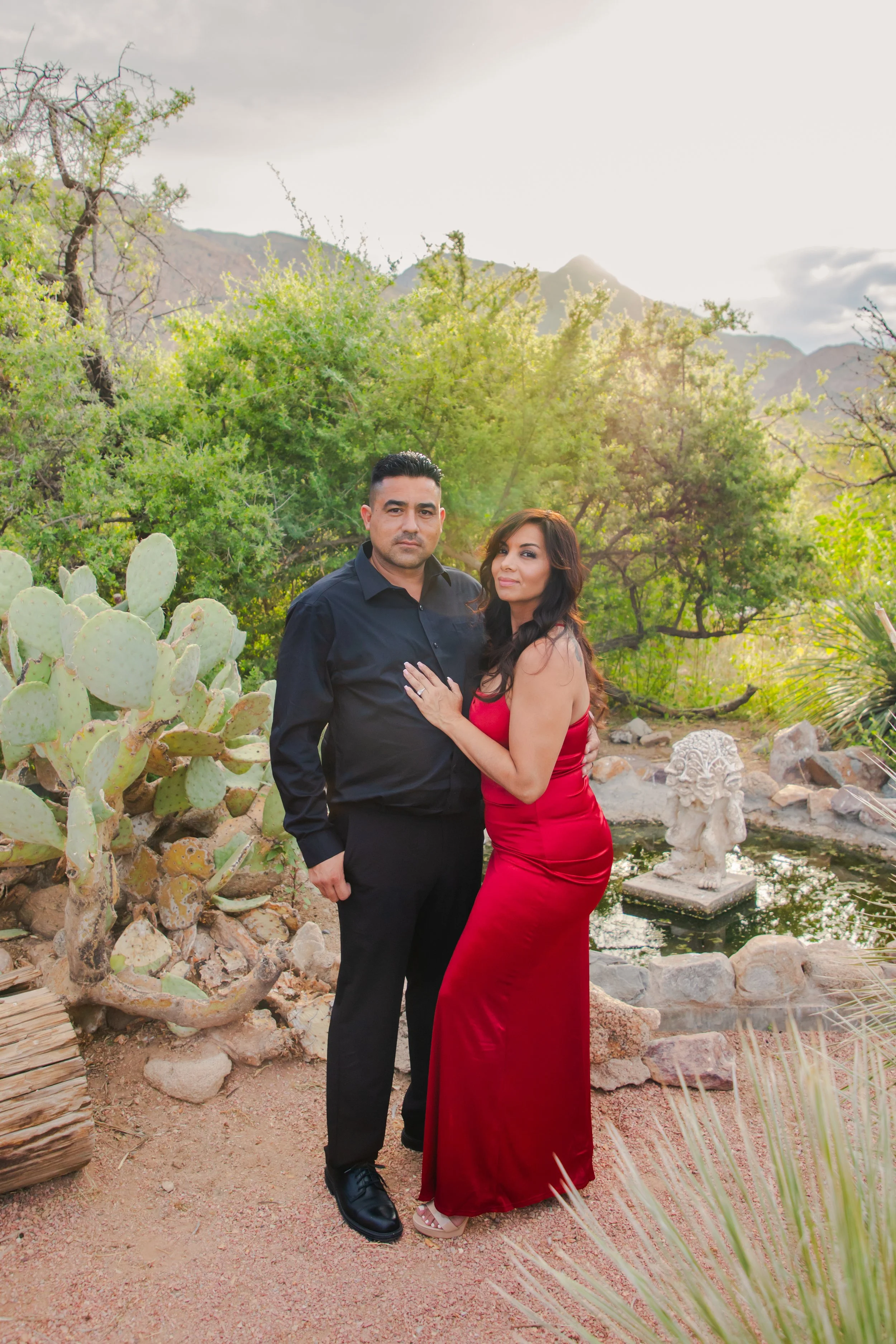 A man in a black shirt and a woman in a red dress standing close together outdoors in the Franklin Mountains near the El Paso Museum of Archaeology.