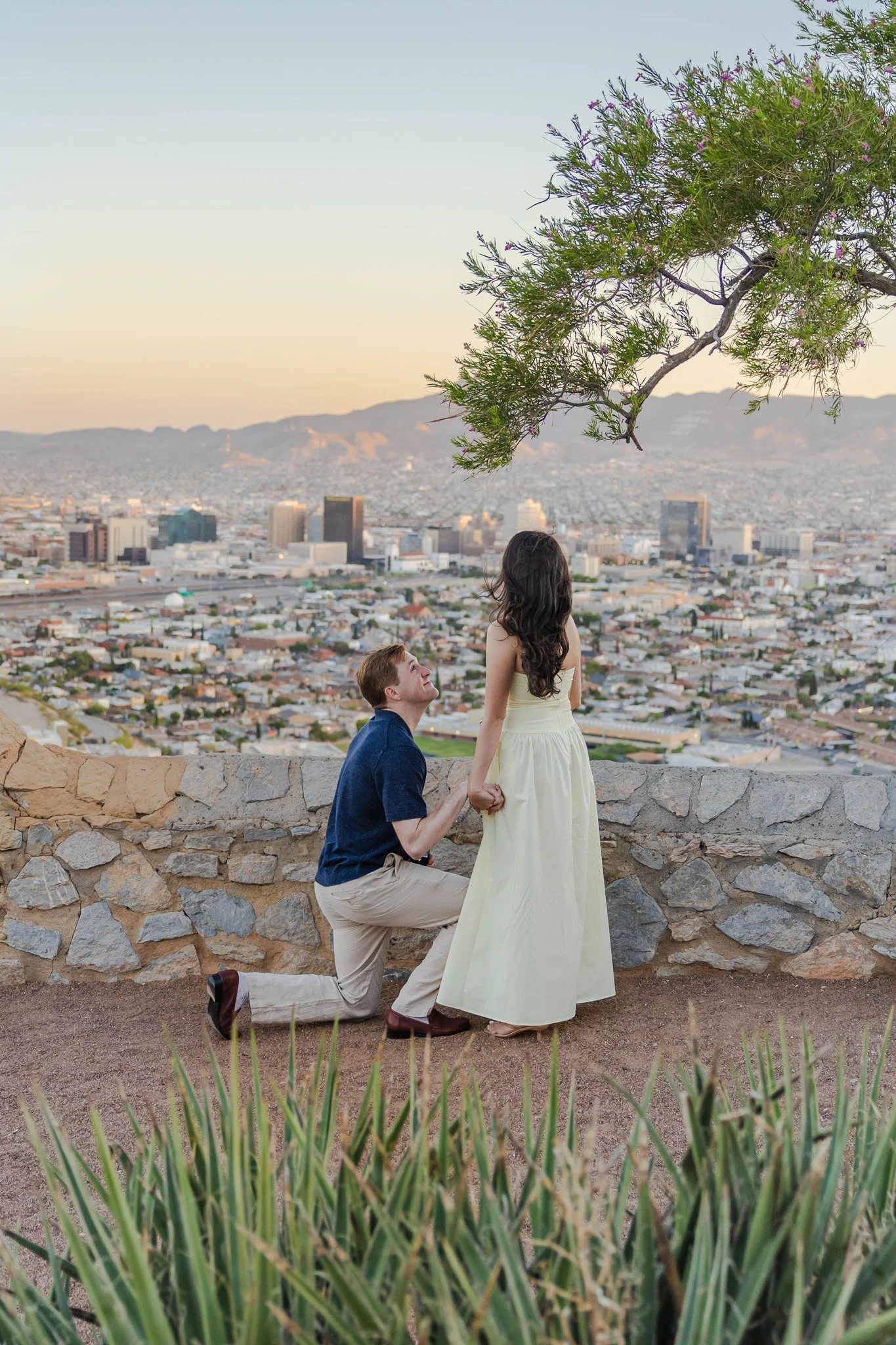 A man proposing to his girlfriend at the Scenic Drive overlook in El Paso, Texas. The man is wearing a blue shirt and khaki pants. The woman is wearing a yellow dress.
