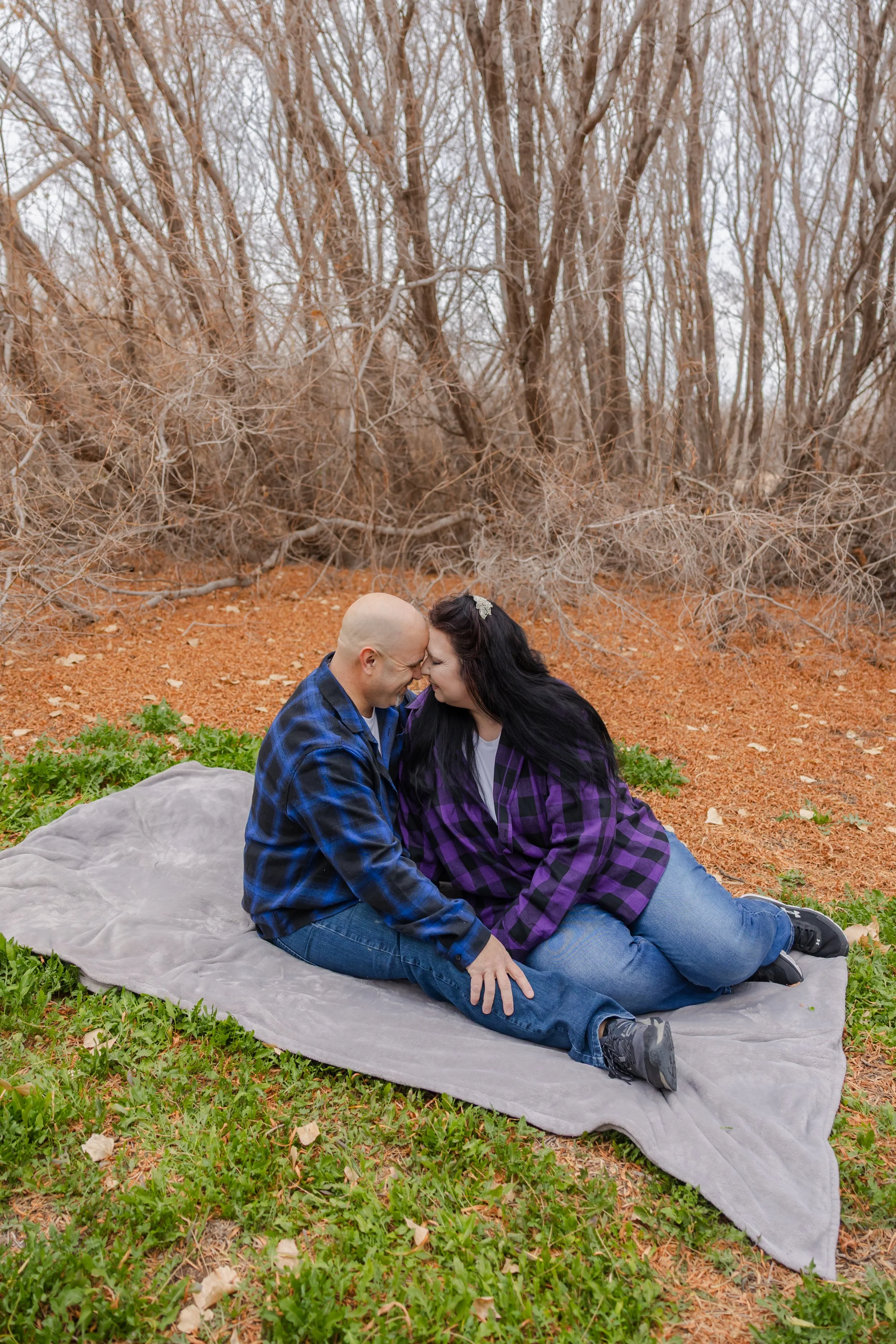 Engaged couple sits at Rio Bosque Park in Socorro, Texas laughing.