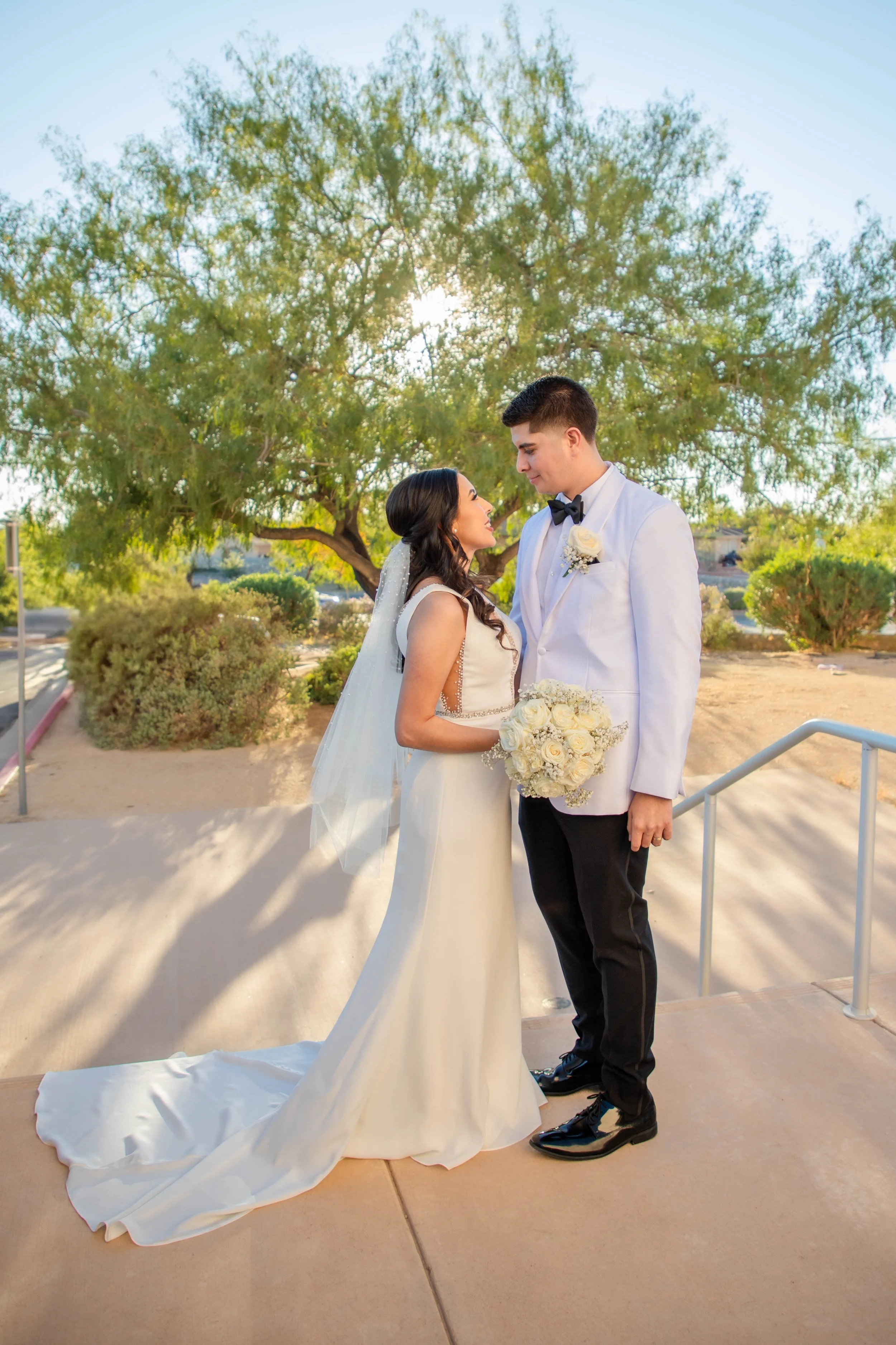 A bride and groom standing outdoors at El Paso's St. Stephens on a sunny day, looking into each other's eyes.