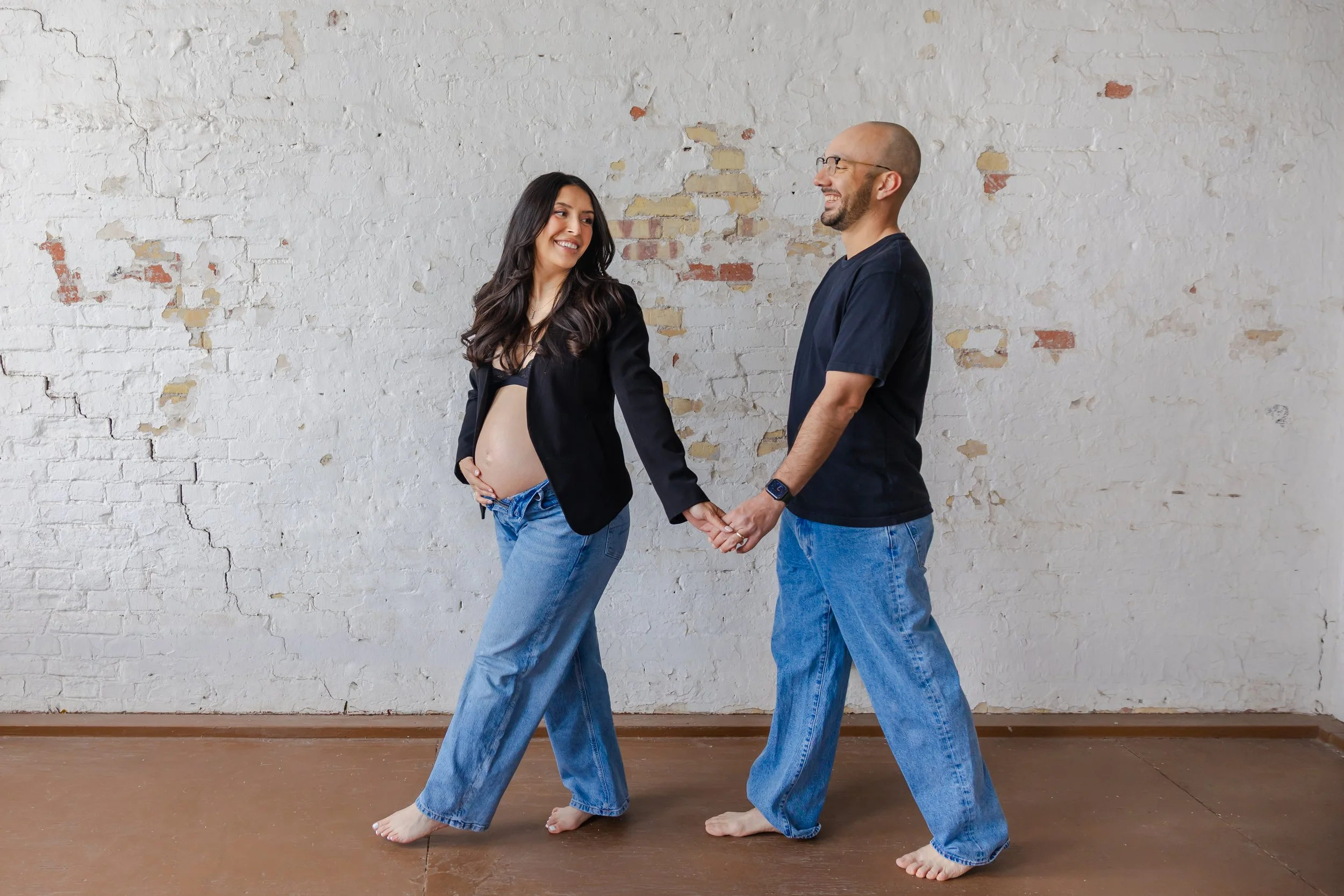 El Paso couple expecting a baby walking in the studio with vintage brick wall..