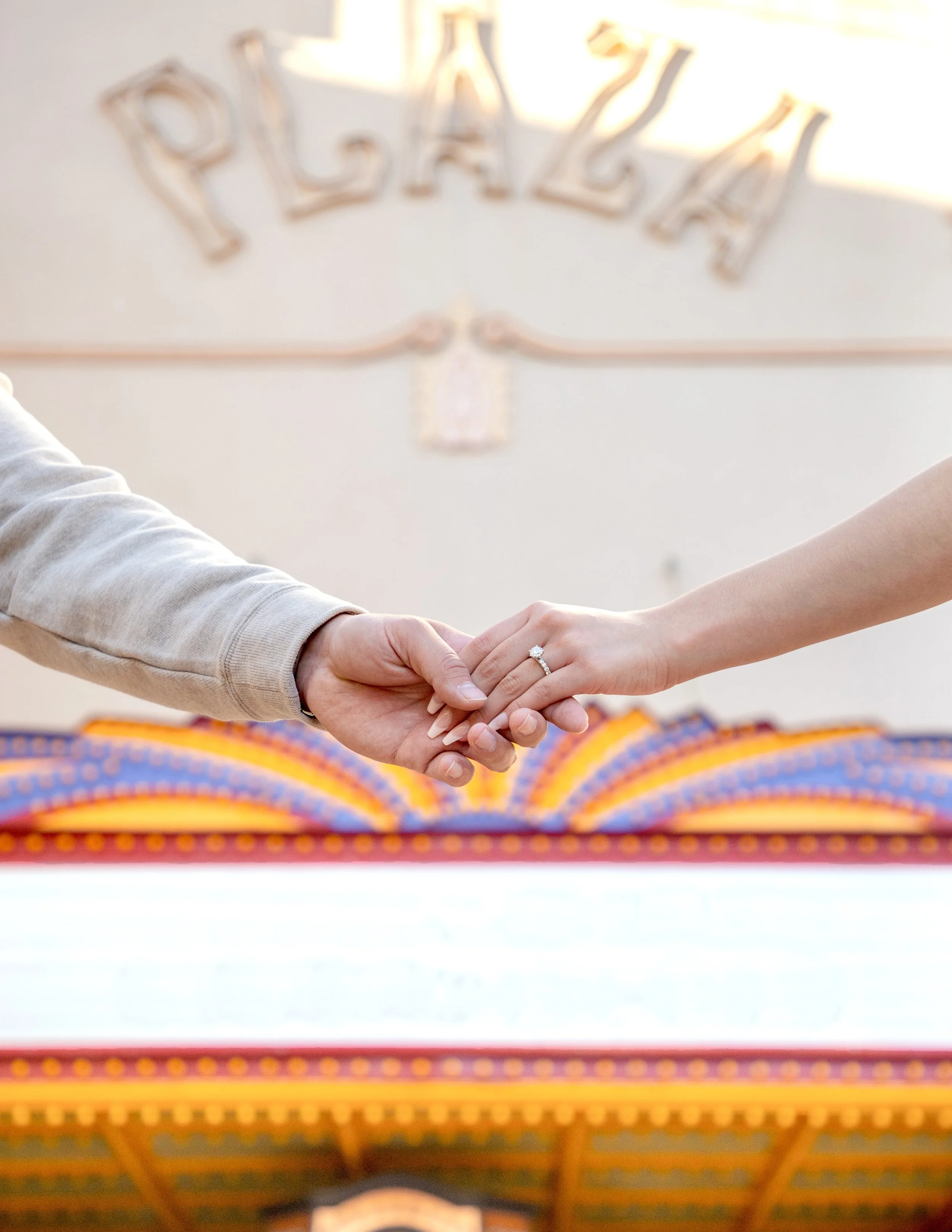 Close-up of a person's hand with a wedding ring holding another person's hand, with El Paso's Plaza Theatre in the background.