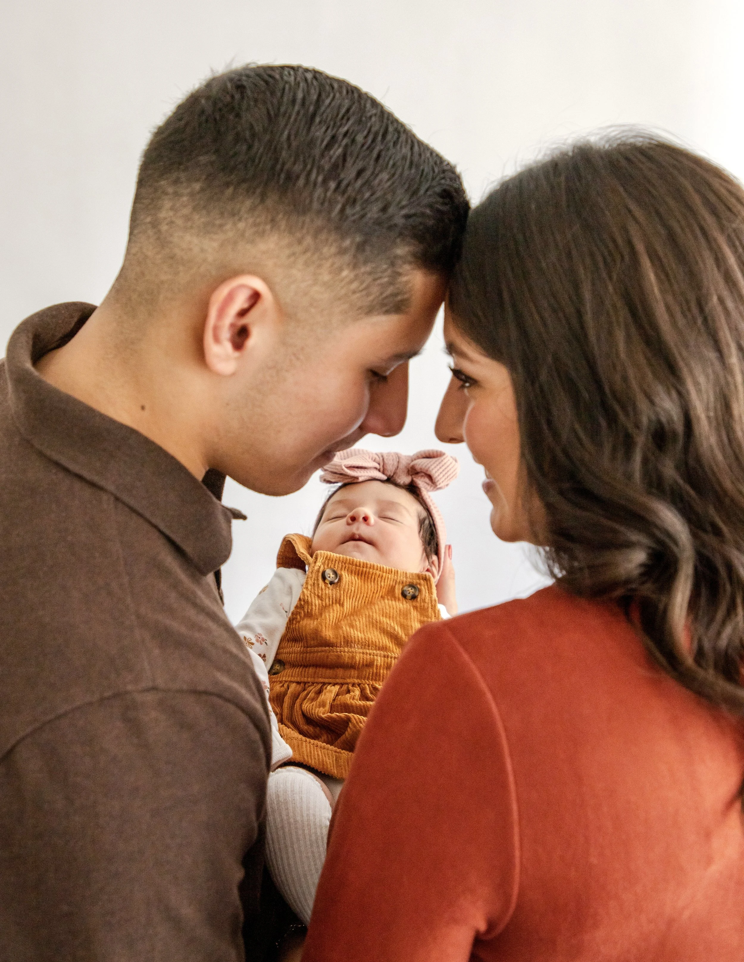 A family of three, with a mother, father, and baby, are touching foreheads together.