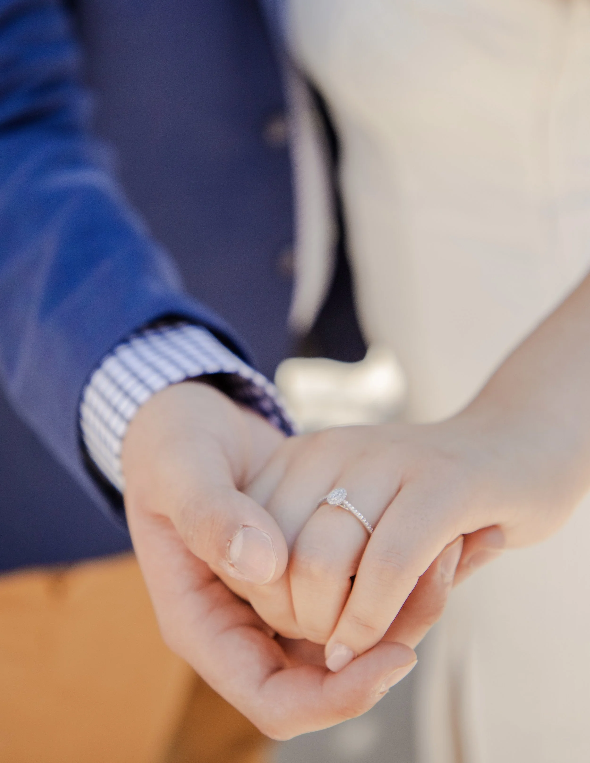 Close-up of two people holding hands, one wearing a diamond engagement ring on the ring finger.