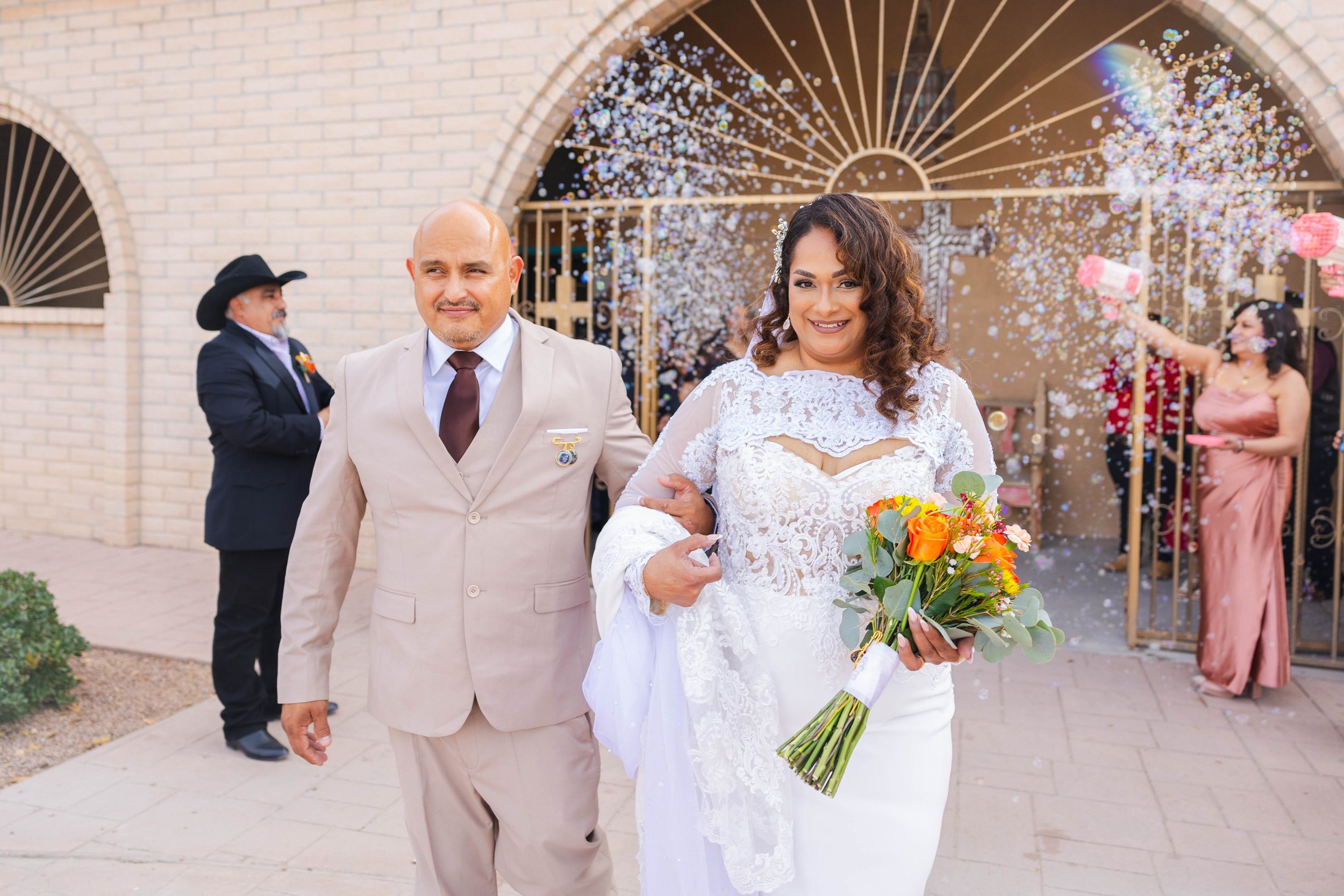 A bride and groom walking out of a Montana Church after a wedding ceremony, with guests celebrating and throwing flower petals in the background.