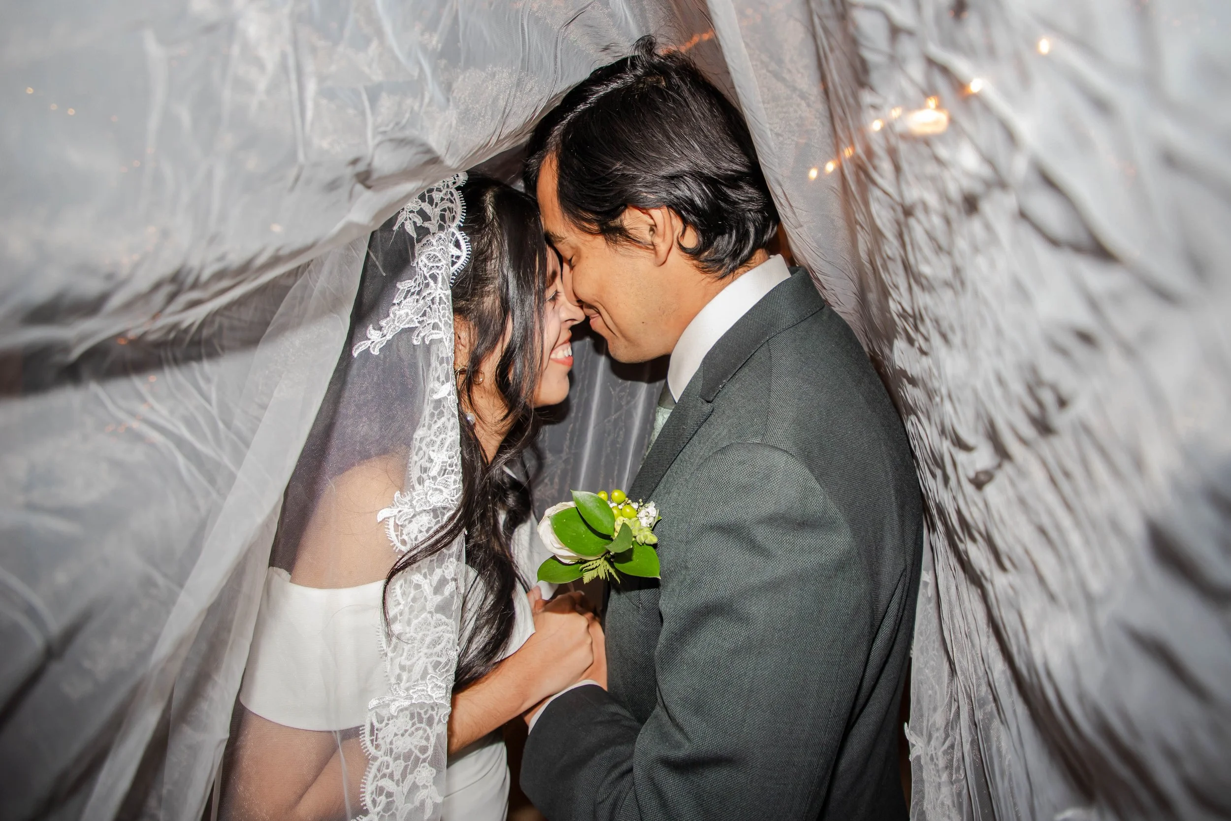 An El Paso newlywed couple sharing a close, intimate moment under a lace and tulle wedding veil, with the bride holding a bouquet of white flowers and greenery at Keystone Heritage Park.
