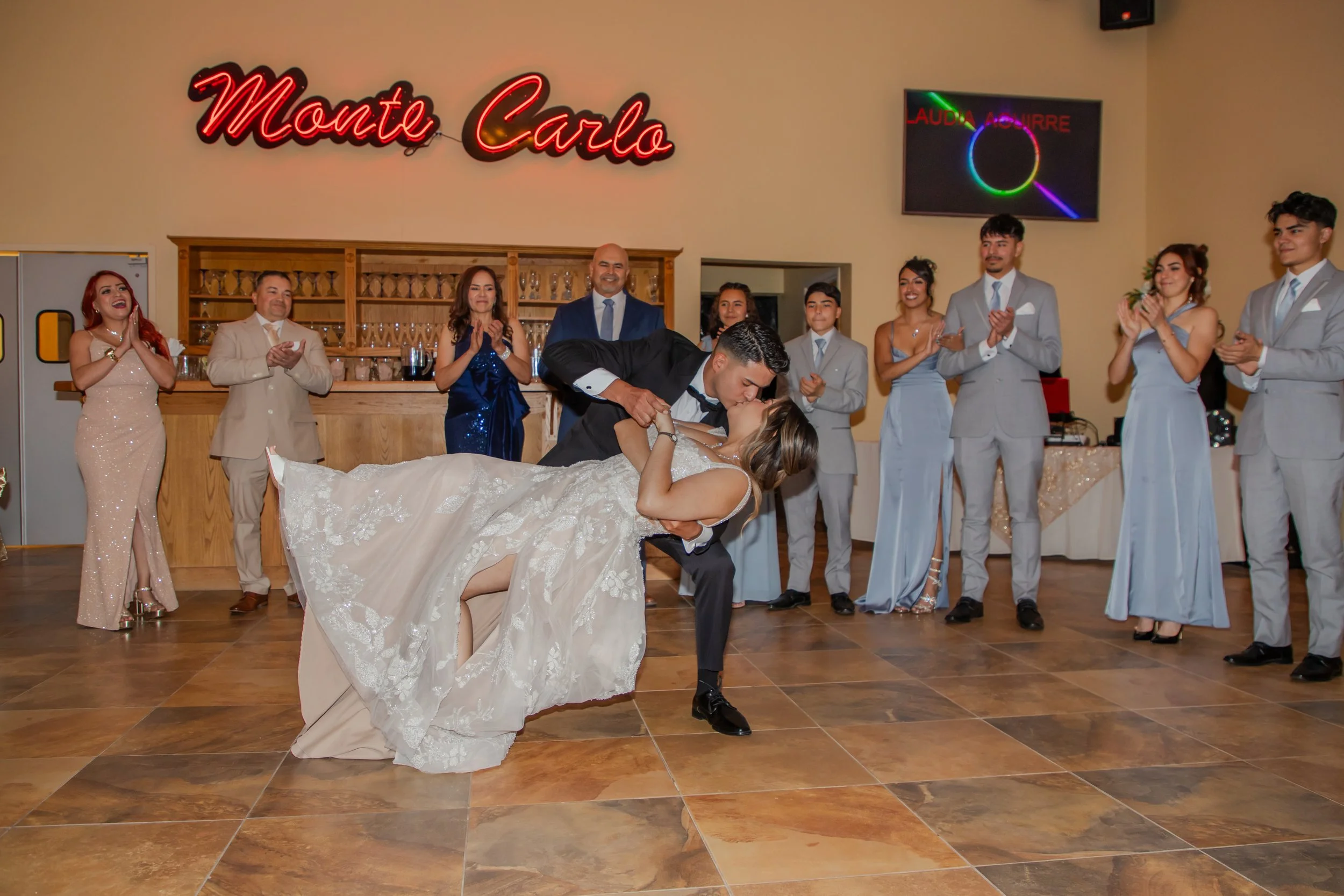 Wedding reception scene at El Paso's Monte Carlo venue with a bride and groom dancing while others clapping around them, in a decorated room with a sign in the back.