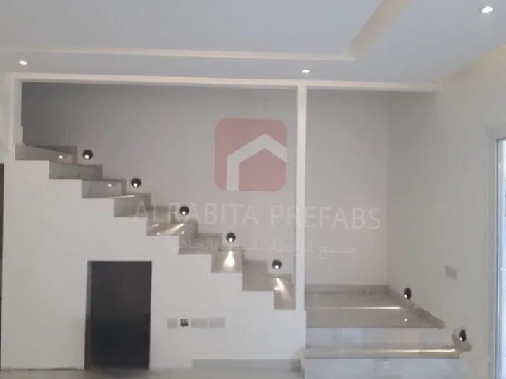 Modern interior space of a prefabricated house with white stairs featuring built-in spotlights executed by Alrabita Prefab Co. اعمال ديكورات داخلية لبيت جاهز مع درج داخلي بإضاءة جانبية مميزة تم تنفيذه من قبل مصنع الرابطة للبيوت الجاهزة