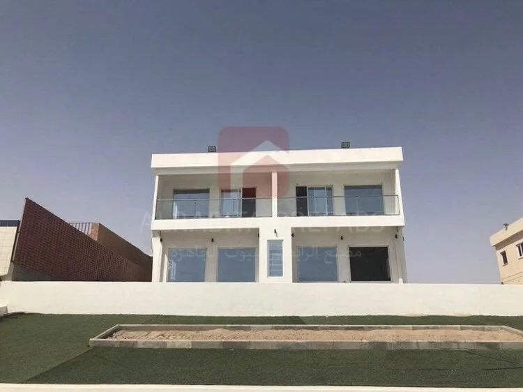 Modern white two-story prefabricated house with large windows, glass balcony railings, and a flat roof executed by Alrabita Prefab Co. بيت جاهز دورين بتصميم مودرن وشبابيك كبيرة تم تنفيذه من قبل مصنع الرابطة للبيوت الجاهزة