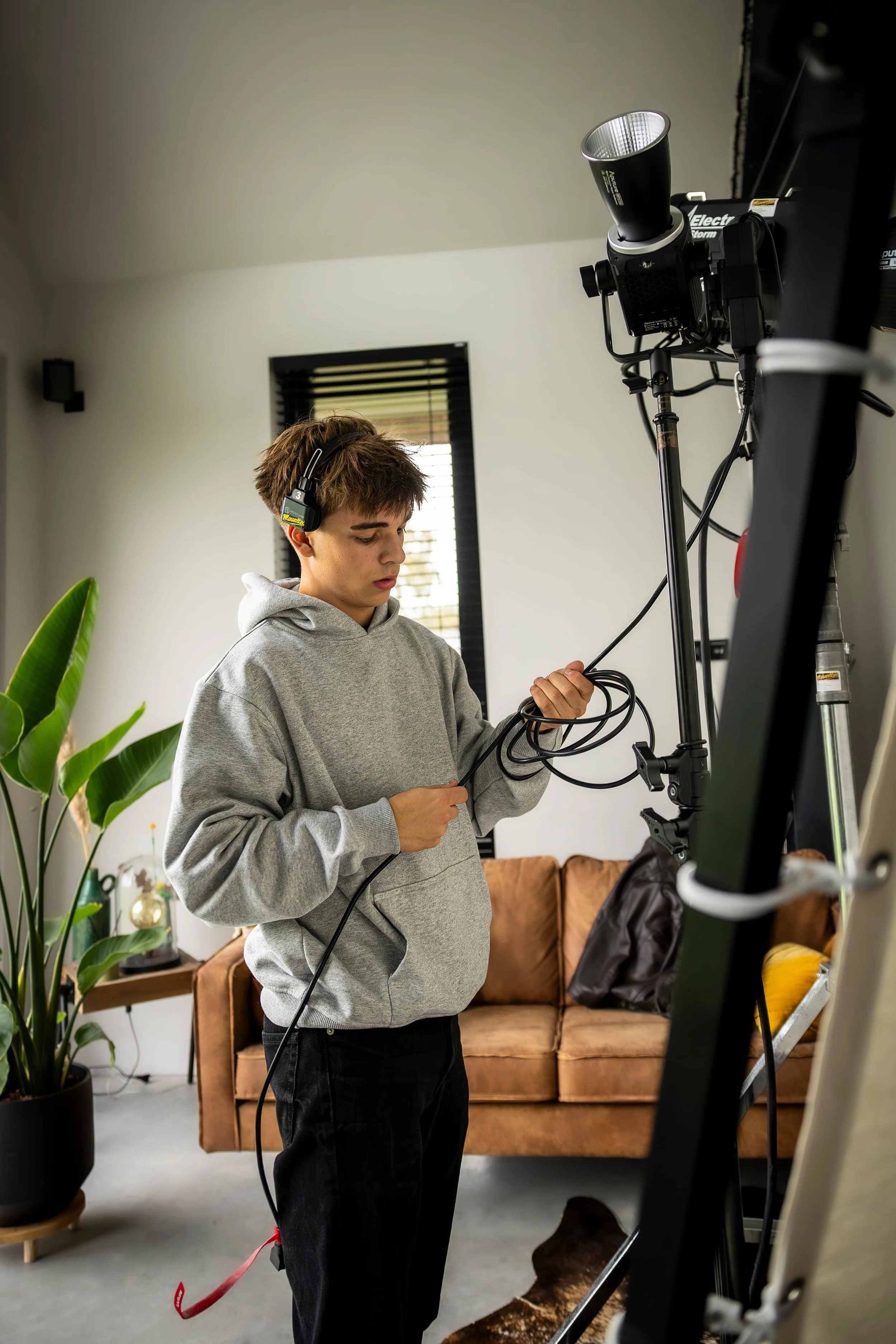 A young man with headphones, wearing a gray hoodie, working with film equipment in a modern, cozy living room.
