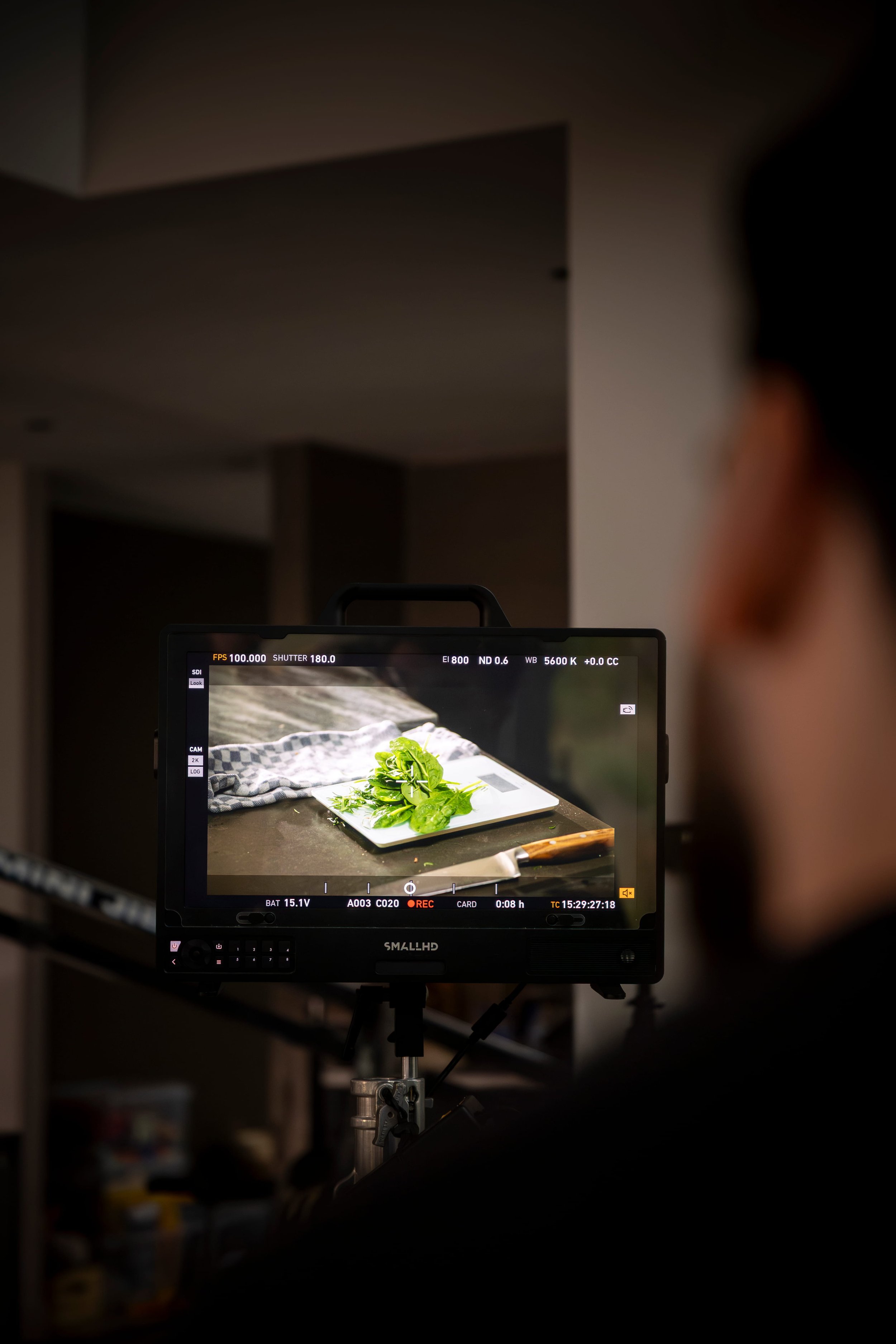 Camera monitor displaying a scene of fresh leafy greens on a white cutting board, with a knife nearby, set on a kitchen countertop.