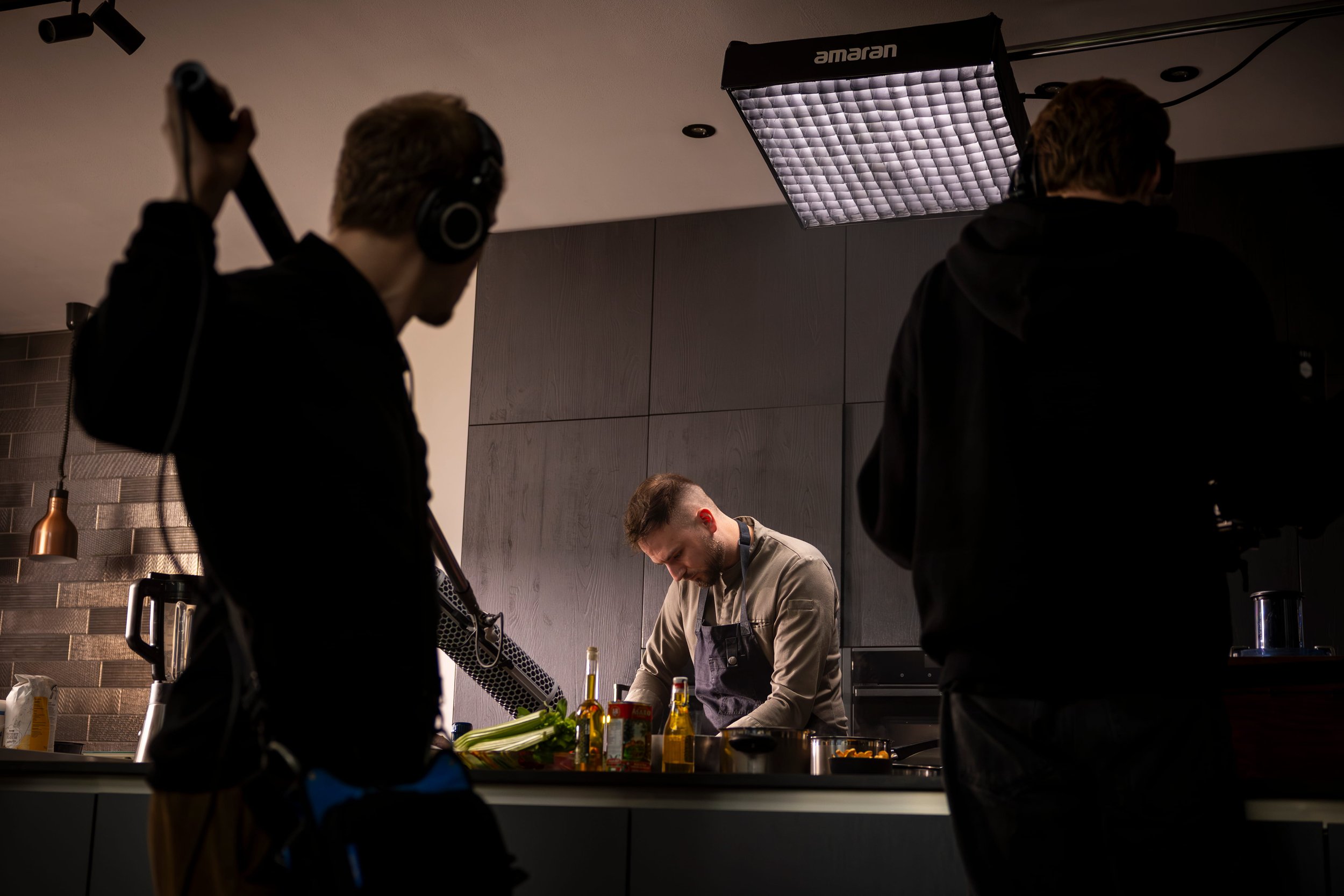 A chef working in a kitchen surrounded by filming equipment and crew, with two crew members filming him.