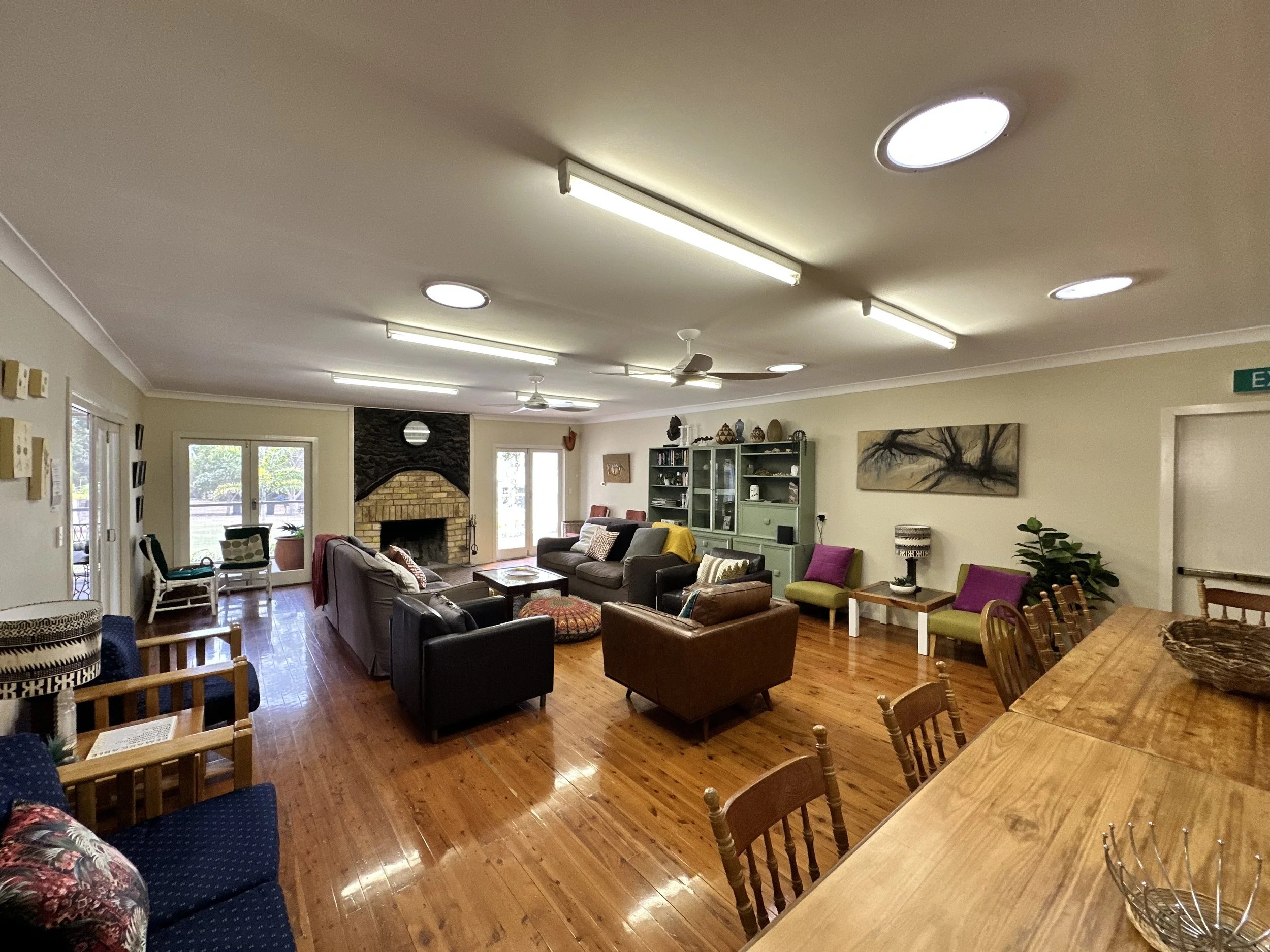 Living room with hardwood floors, multiple couches, a fireplace, large windows, and various chairs with pillows, a green cabinet, and wall art.