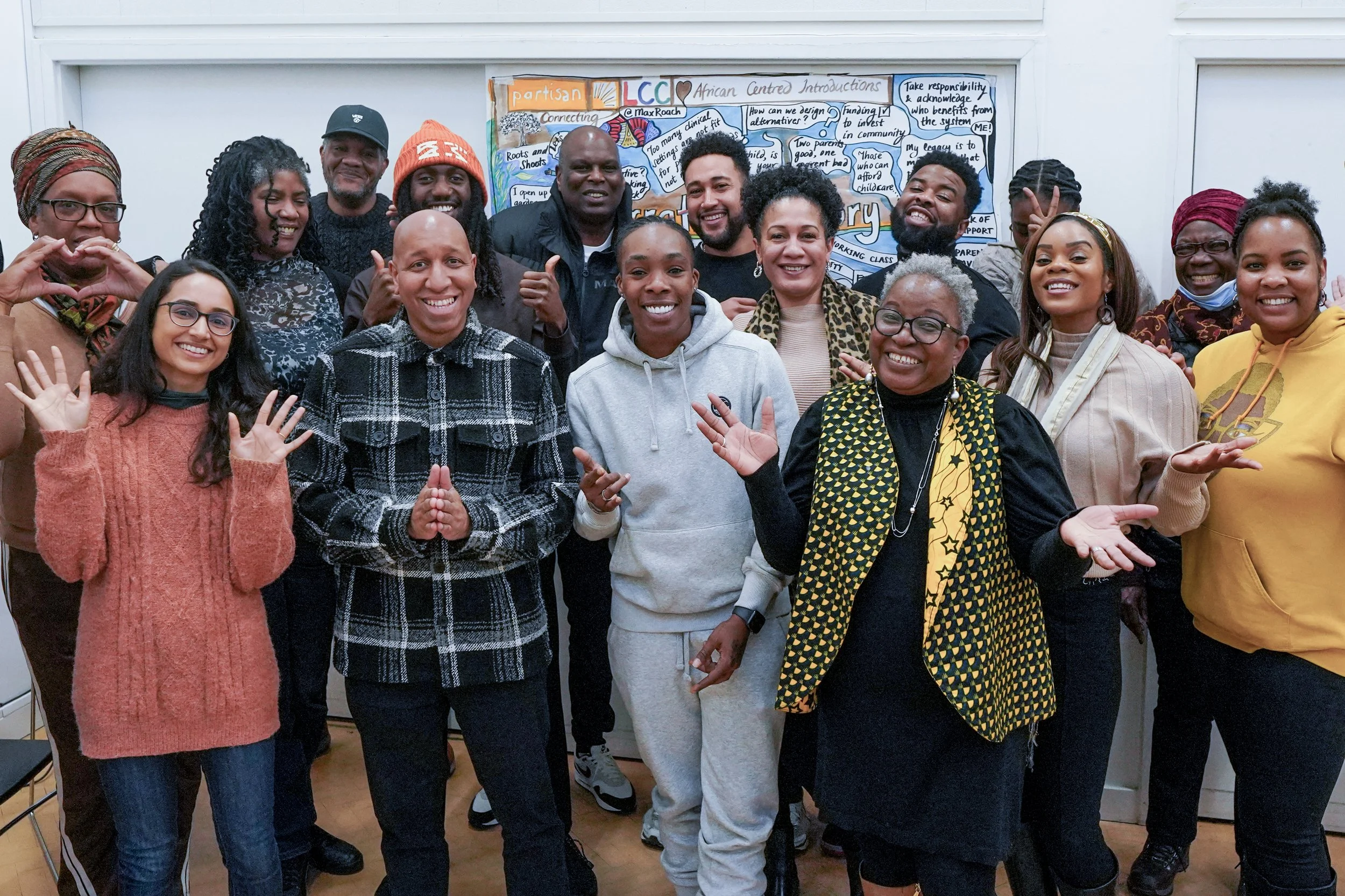 Group of diverse people smiling and posing together in front of a colorful community board.