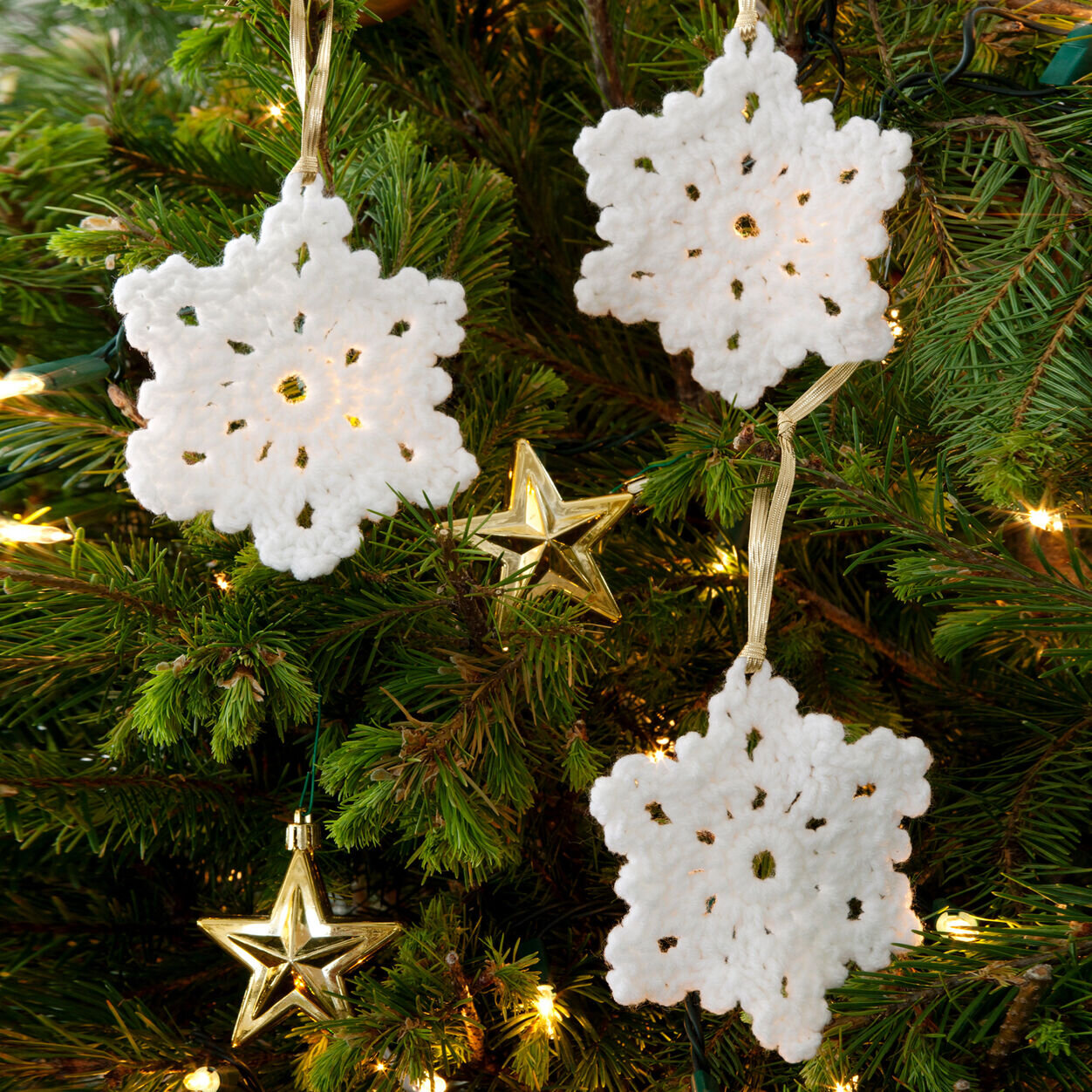 three crochet snowflake ornaments hanging on a tree
