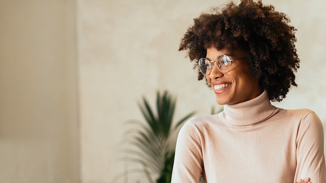 Person with curly hair wearing glasses and a turtleneck, smiling.