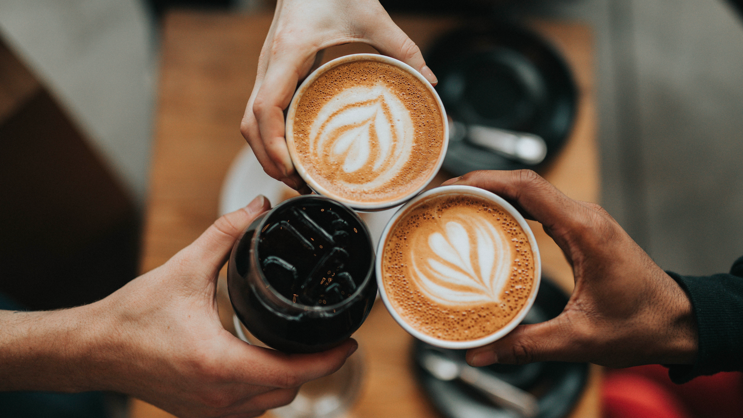 3 hands holding coffee beverages