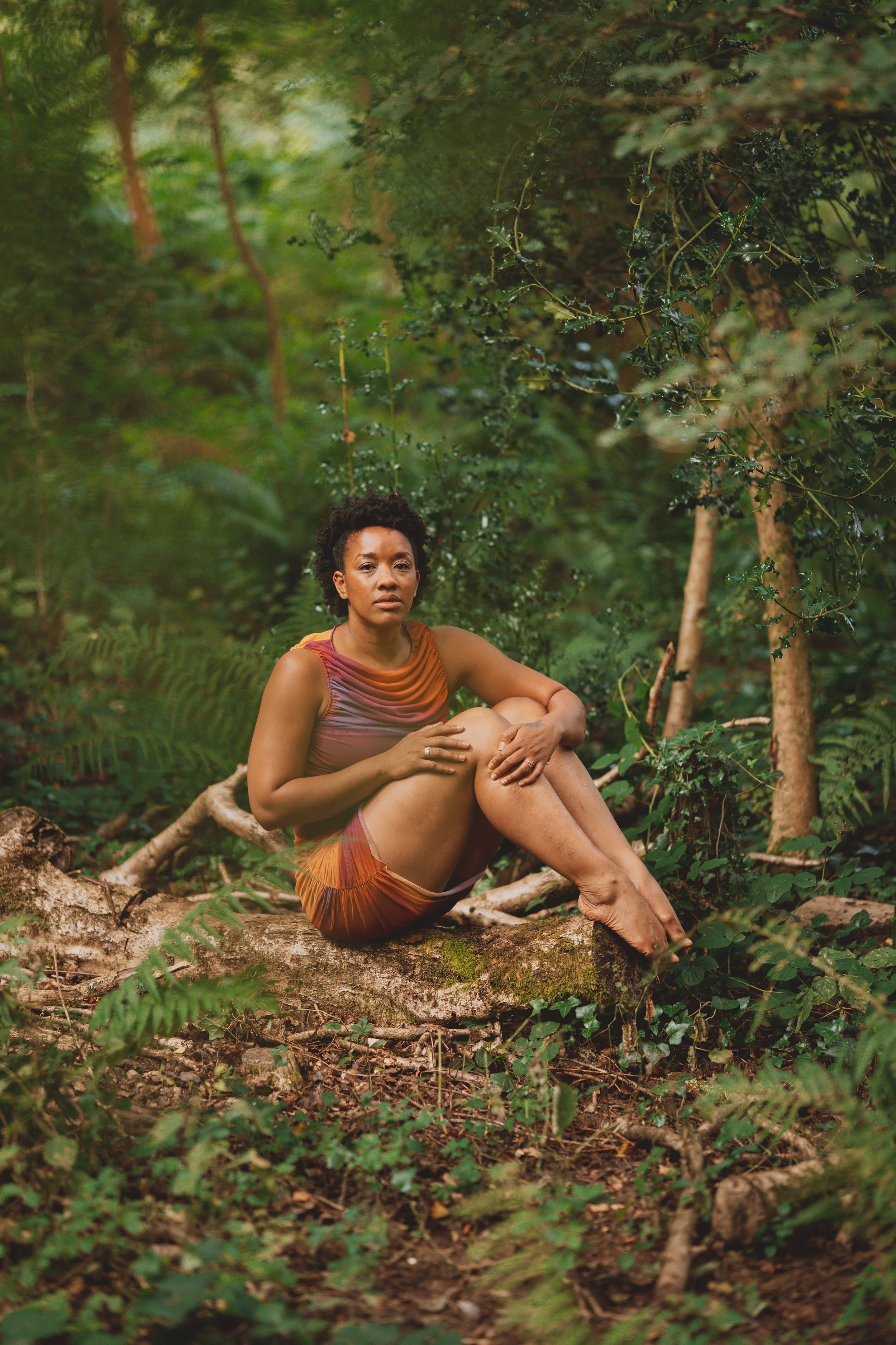 She sits on a moss-covered log staring directly at you, hugging her legs to her chest as her fingers press into her legs.