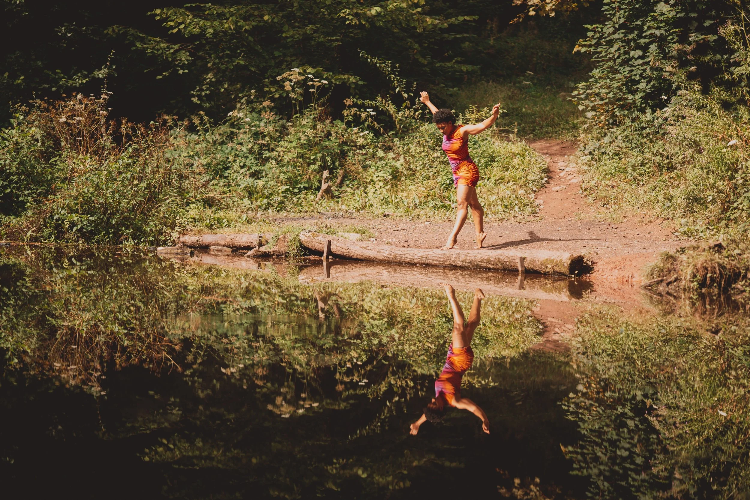 Again she stands far from you. Between you and her rests a lake. She stands in the soil beside the lake on her toes with wide legs and arms reaching wide toward the sky. Her face studies the intricate reflection of her body in the water.