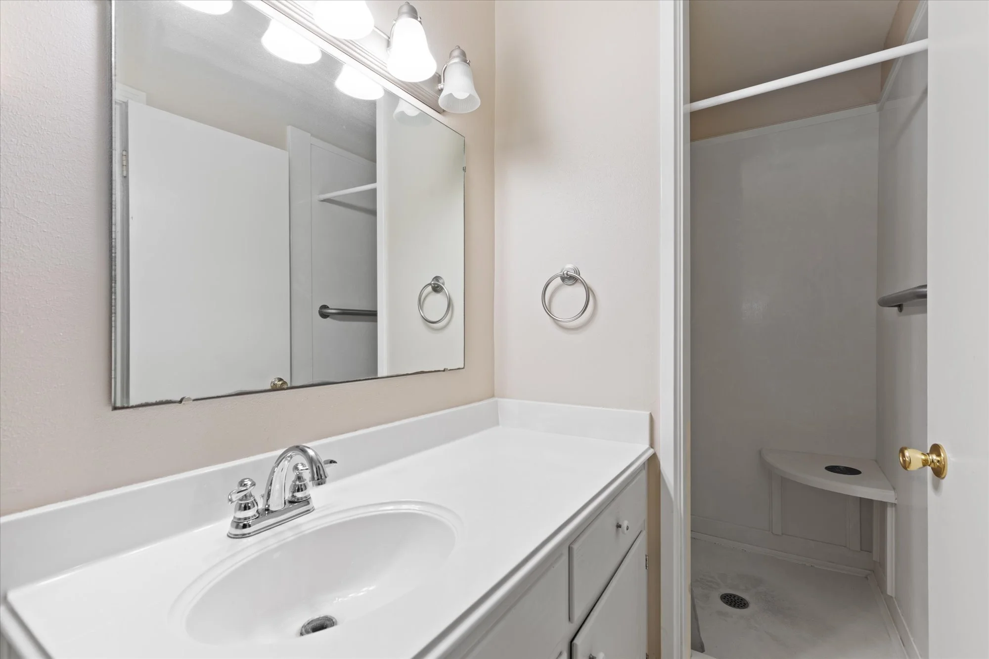 Bathroom with white vanity sink, mirror, and a separate shower area with a bench and towel rack.
