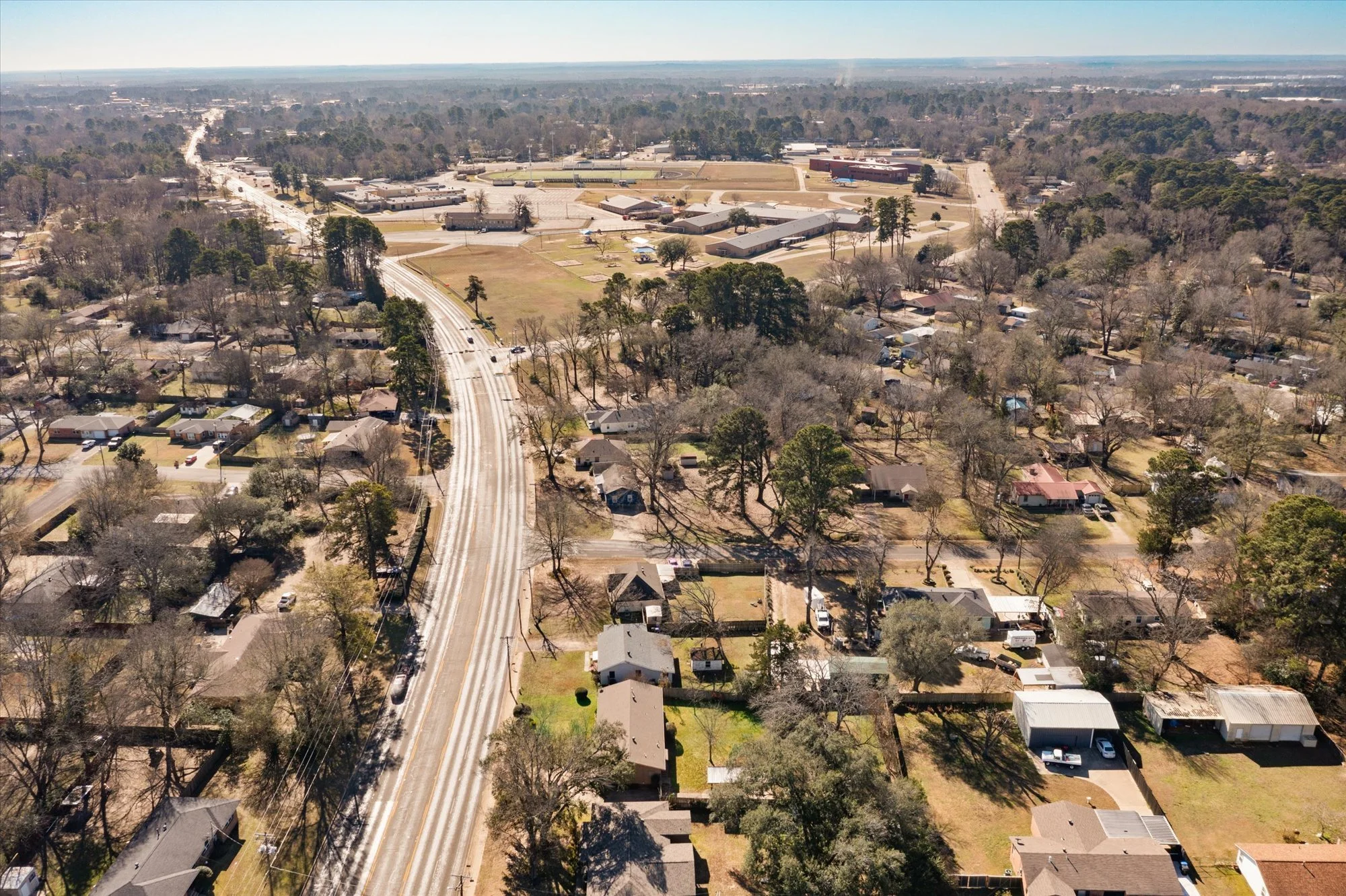 Aerial view of a suburban neighborhood with houses, trees, and roads, with a school or large building complex in the background.