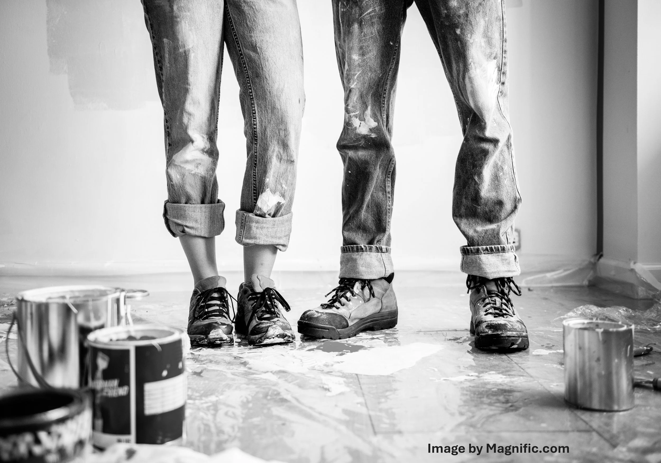 Two individuals' lower bodies standing on a paint-splattered floor, surrounded by paint cans, in a black and white image.