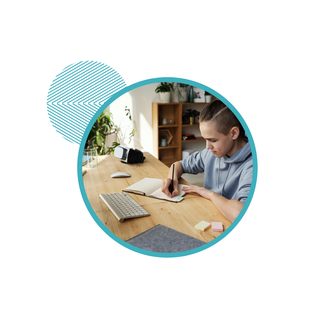 Person writing in notebook at a desk with keyboard and mouse, in a home office setting.