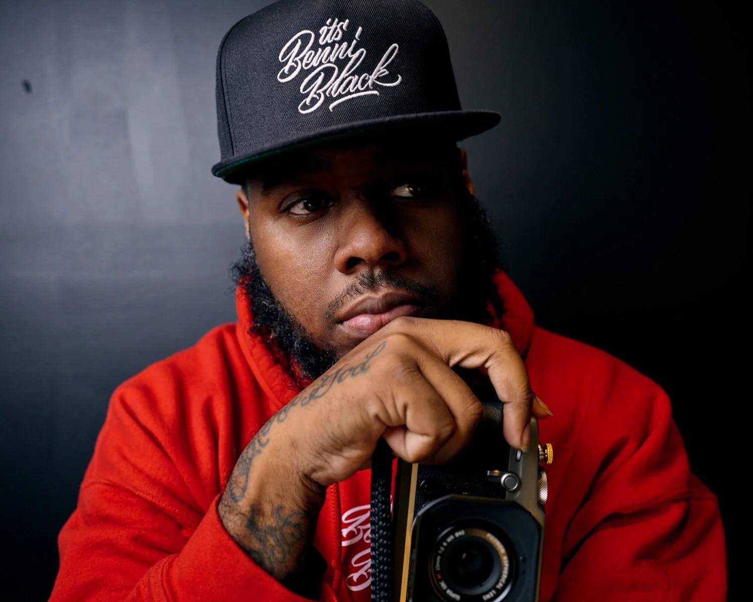 Benni Black wearing a red jacket and black cap, holding a camera