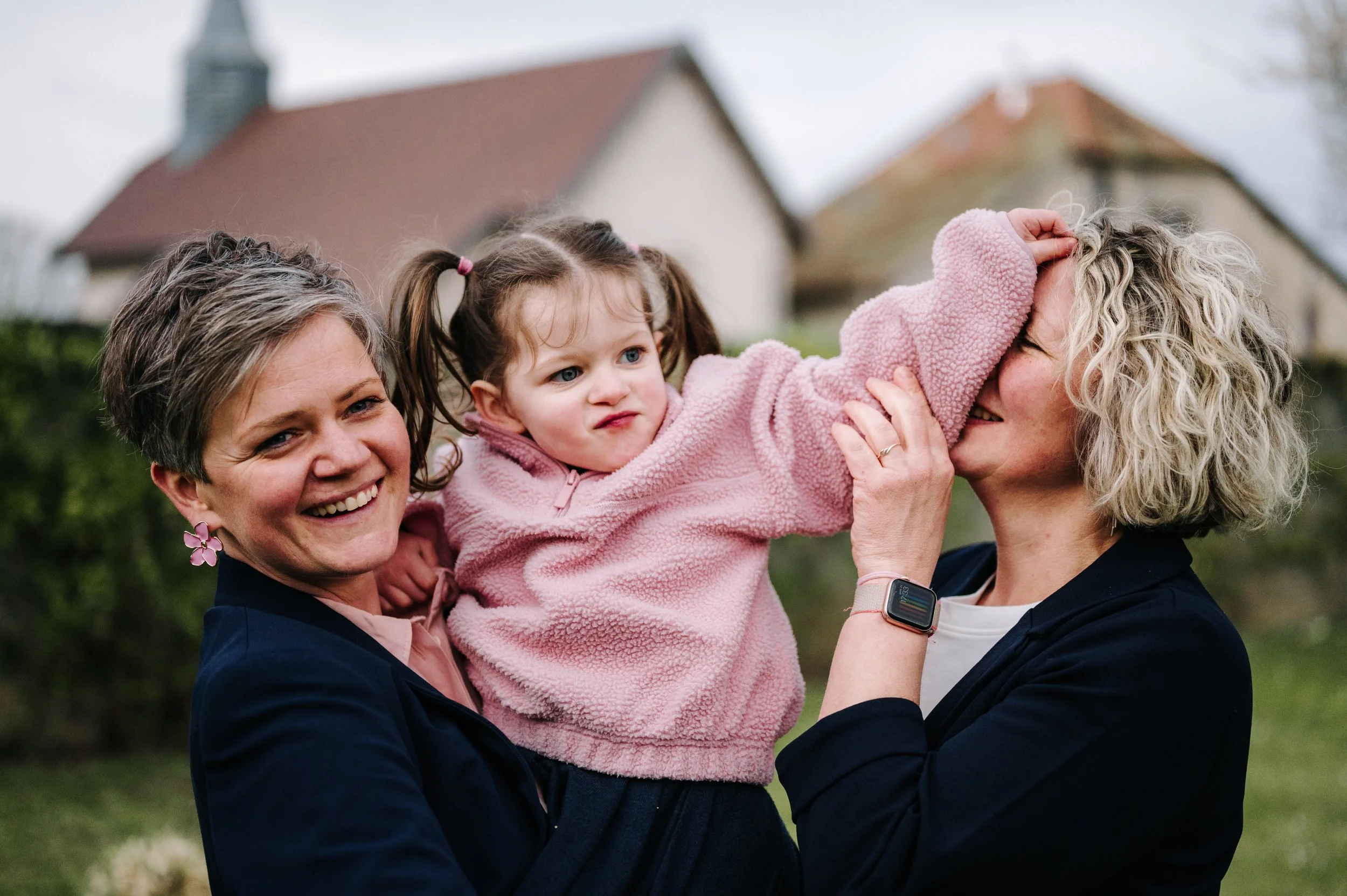 Trois femmes, dont une enfant, joyeusement réunies à l'extérieur, partageant un moment de complicité.