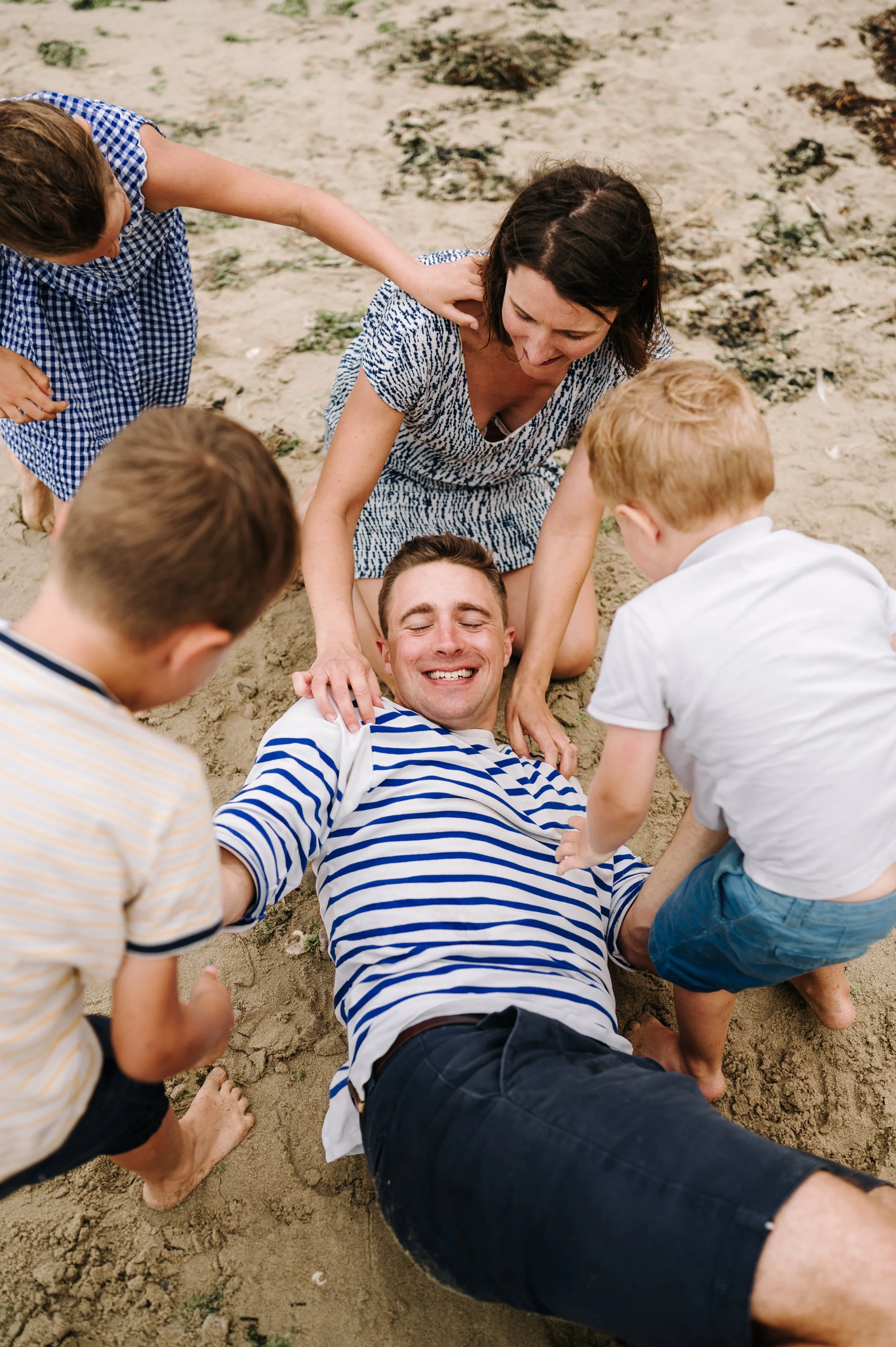 Un groupe d'enfants et une femme jouent et se soutiennent sur la plage, certains étant allongés dans le sable.