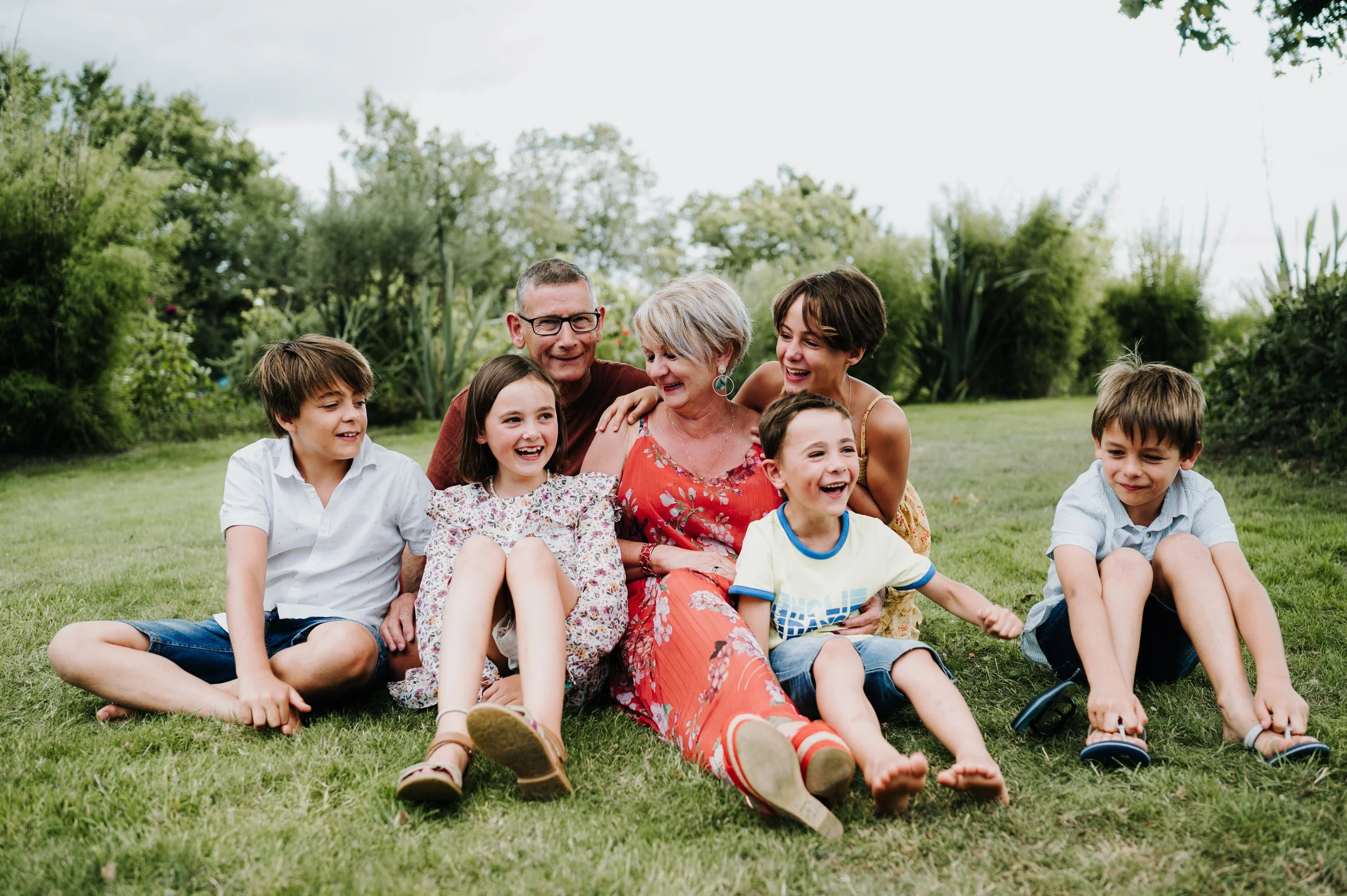 Groupe d'adultes et d'enfants souriants assis sur l'herbe dans un jardin verdoyant en plein air.