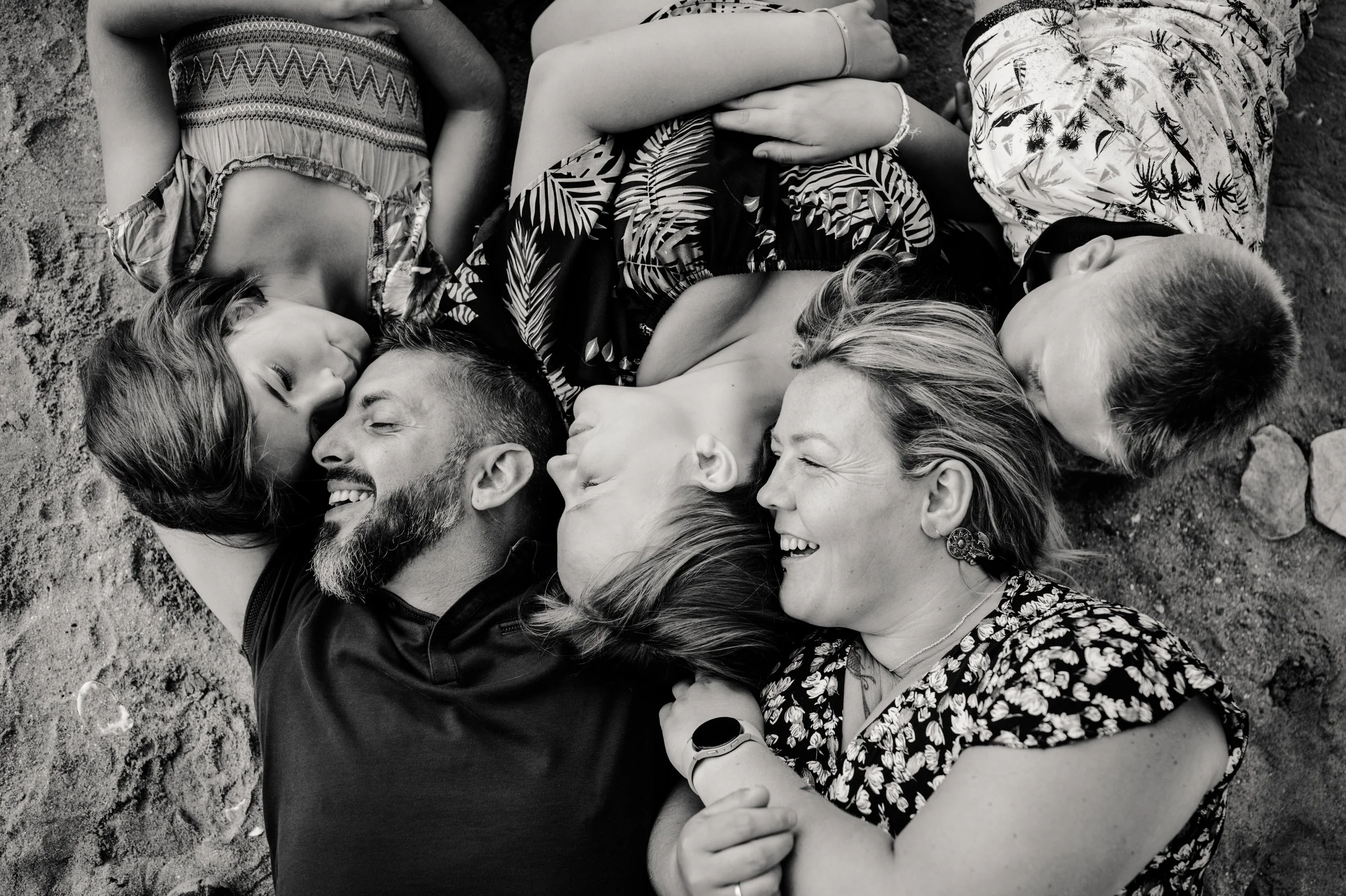 Groupe de personnes allongées sur le sol, partageant un moment de joie et d'amitié, en noir et blanc.